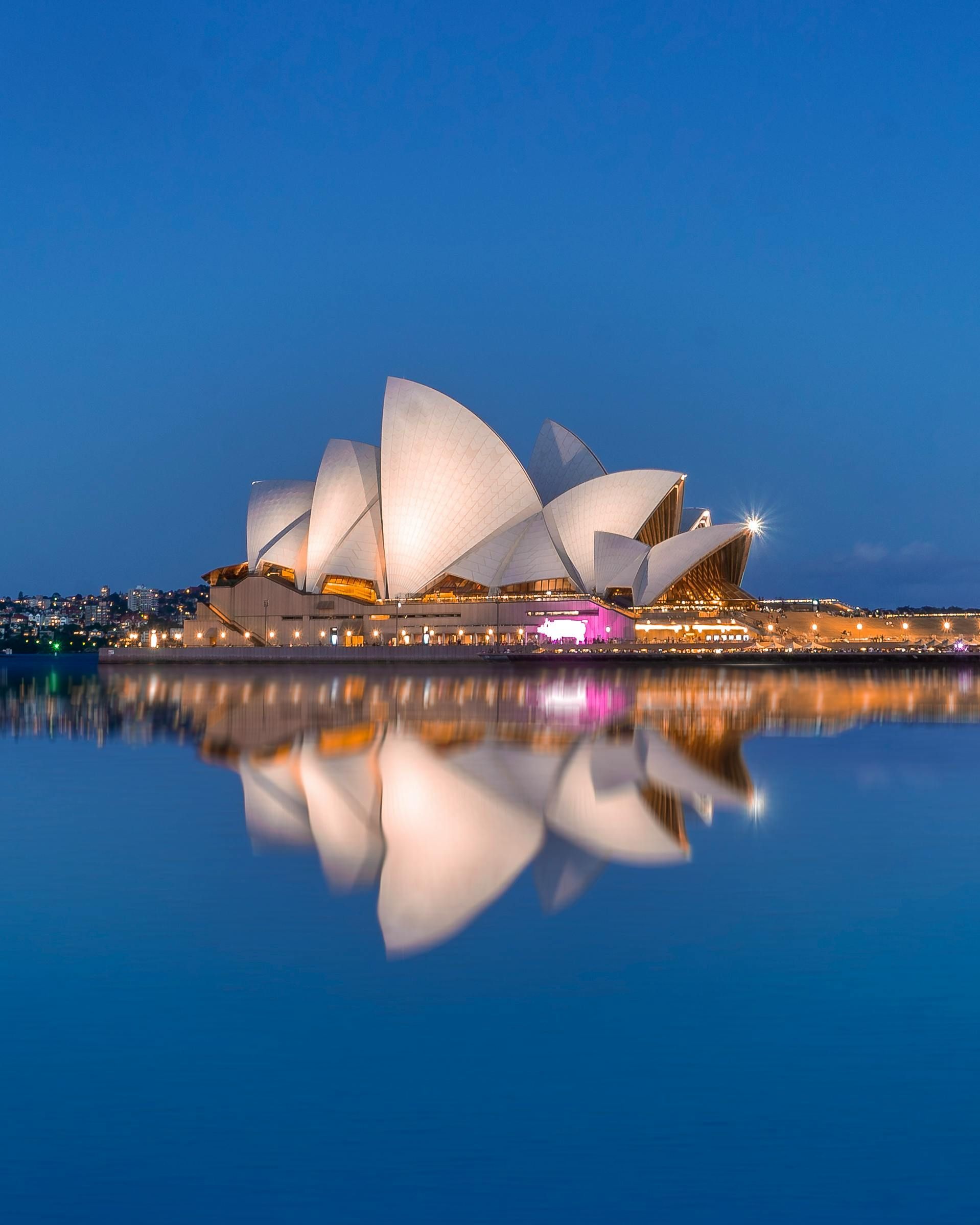 The Sydney opera house is reflected in the water at night.