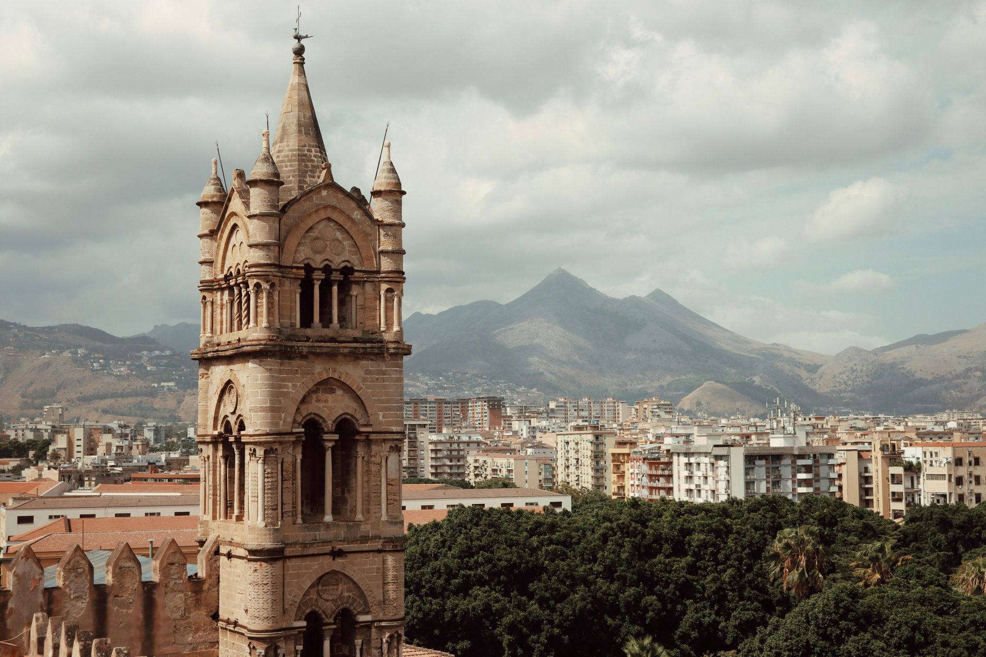 An aerial view of a city with a tower in the foreground and Mount Etna in the background in Sicily, Italy.