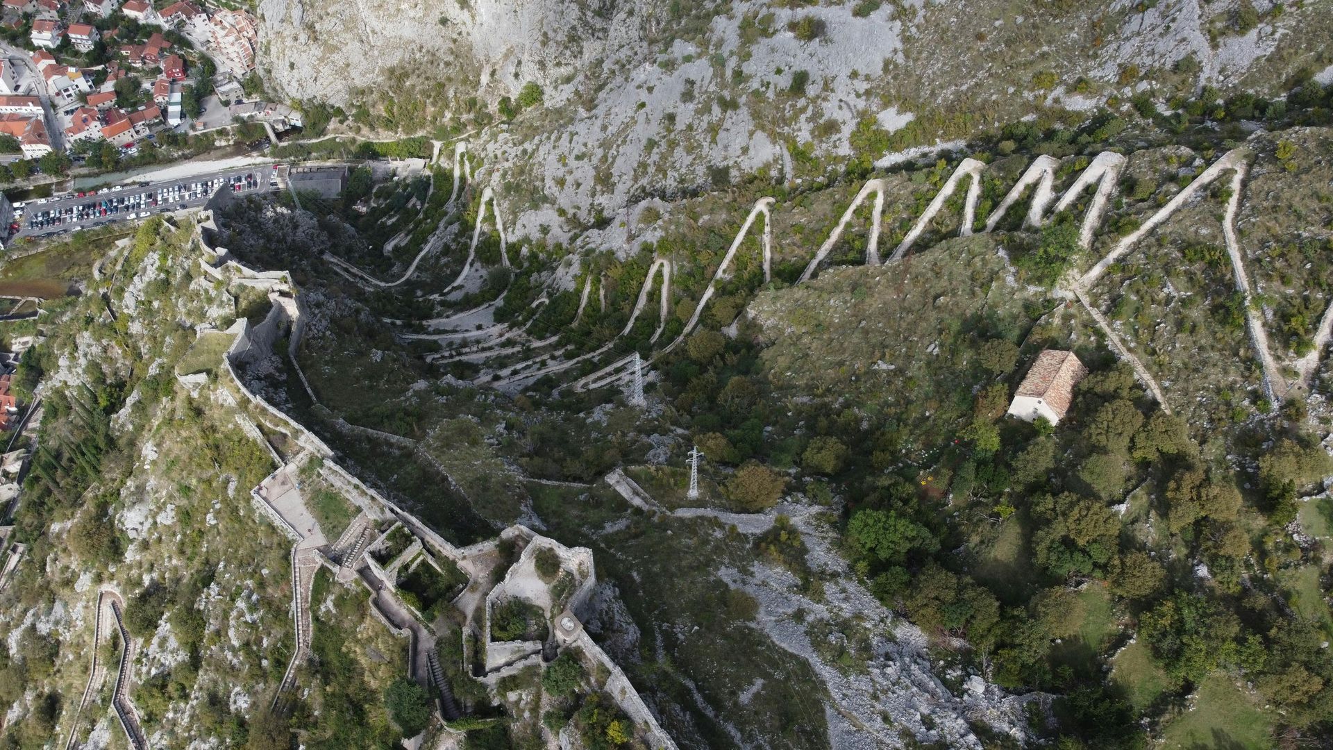 An aerial view of a very winding road on a mountain with the Kotor Fortress along it in Montenegro. 