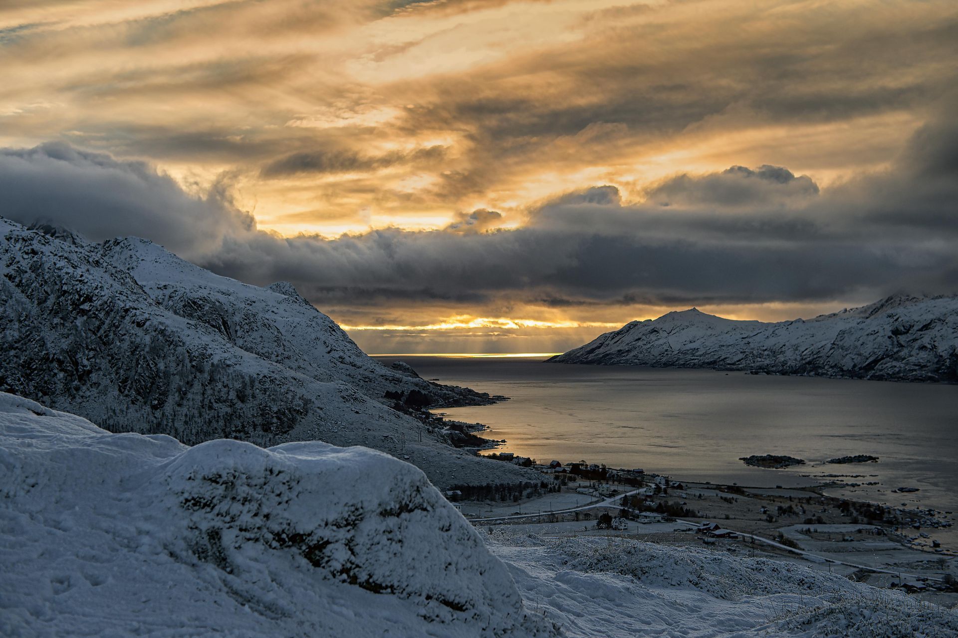 A snowy landscape with a lake and mountains in the background at sunset on the Norwegian Coast.