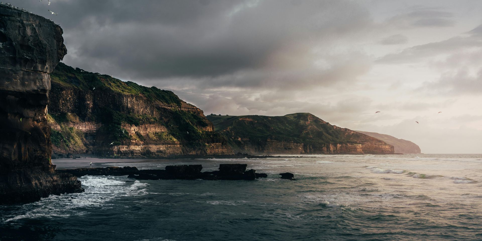 A cliff overlooking a body of water with mountains in the background in New Zeland.