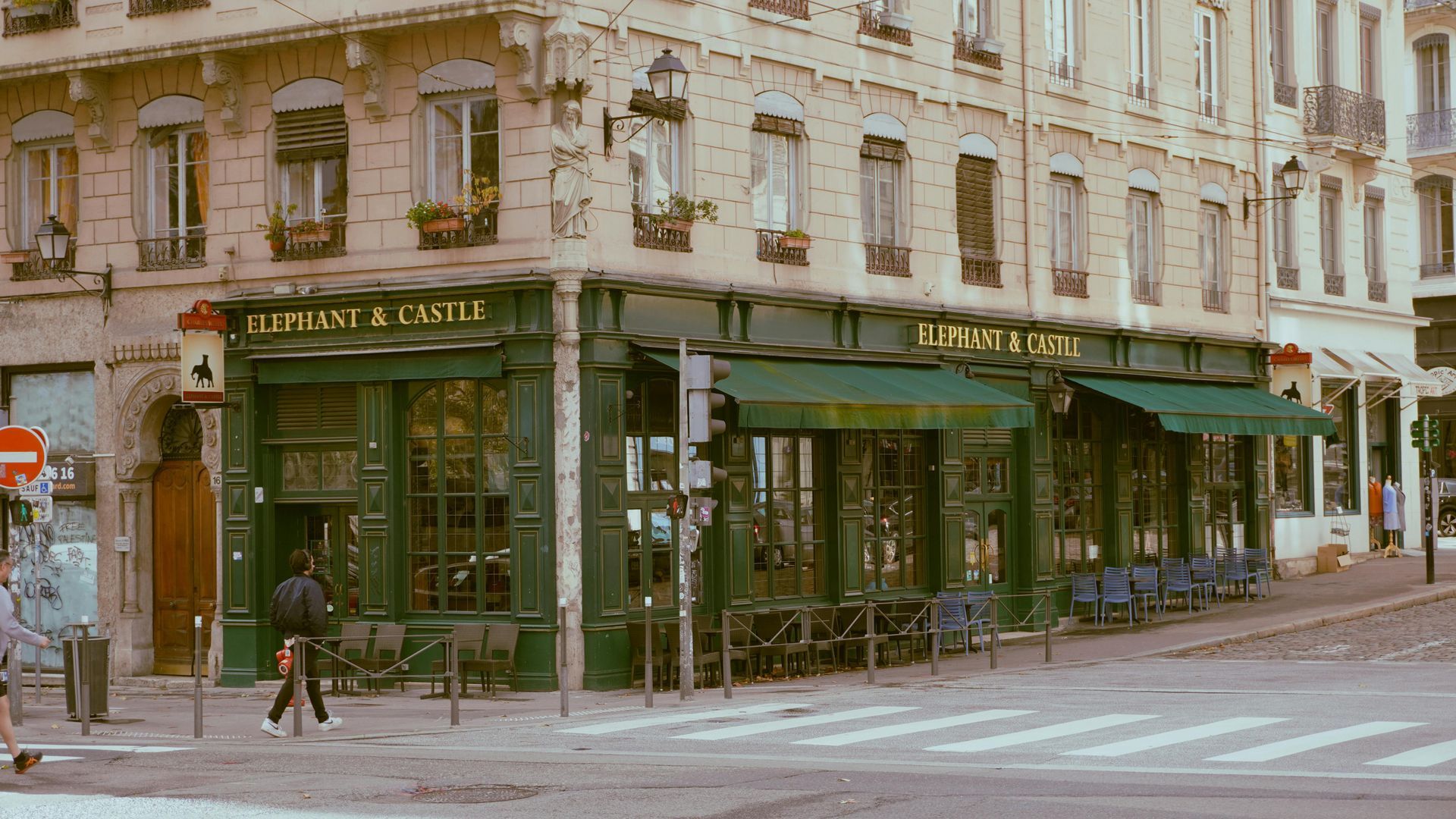 A man is walking down the street in front of a restaurant called elephant & castle. in Lyon, France.