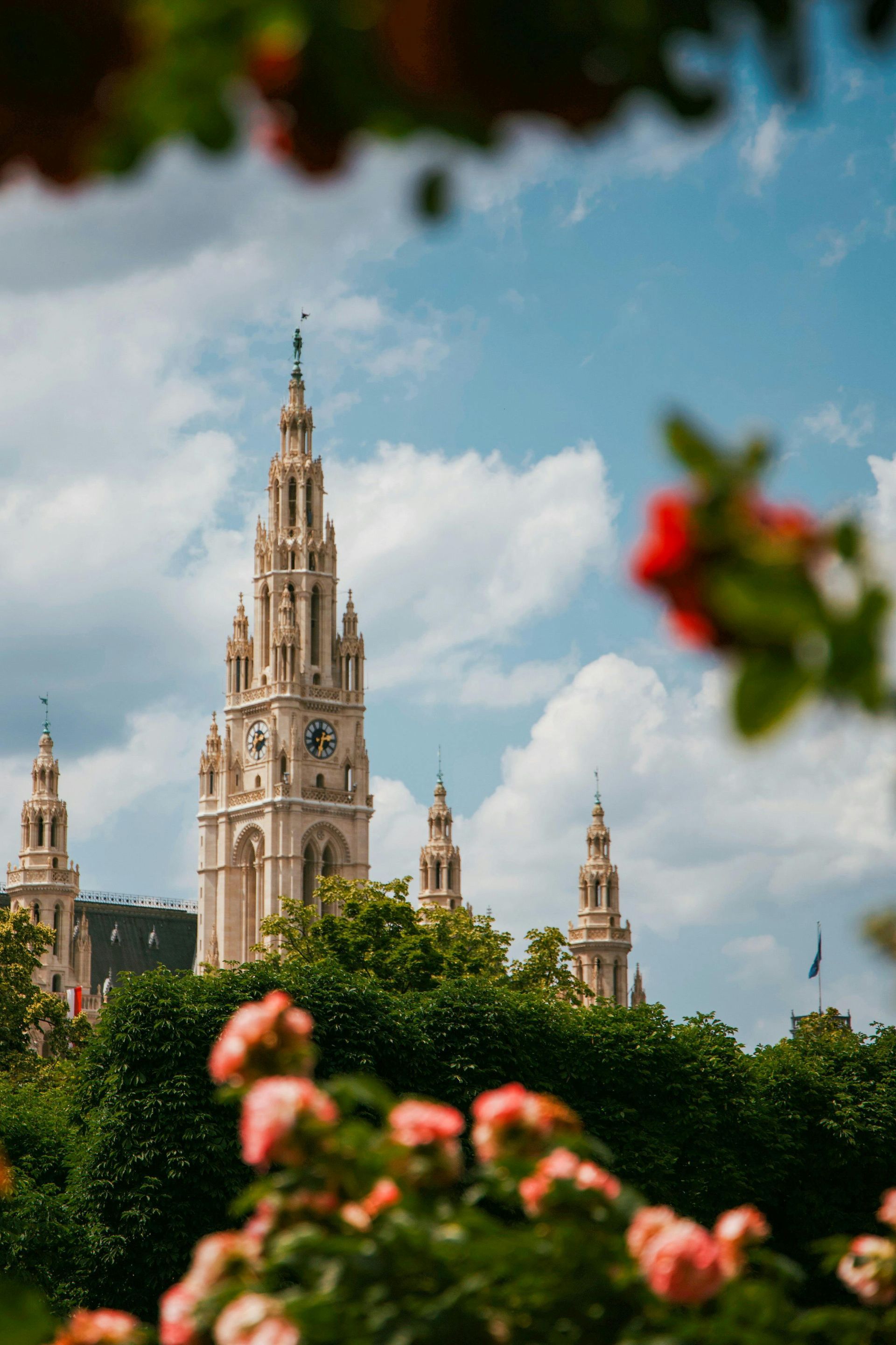 Vienna City Hall with a clock on top of it is surrounded by flowers and trees in Vienna, Austria.