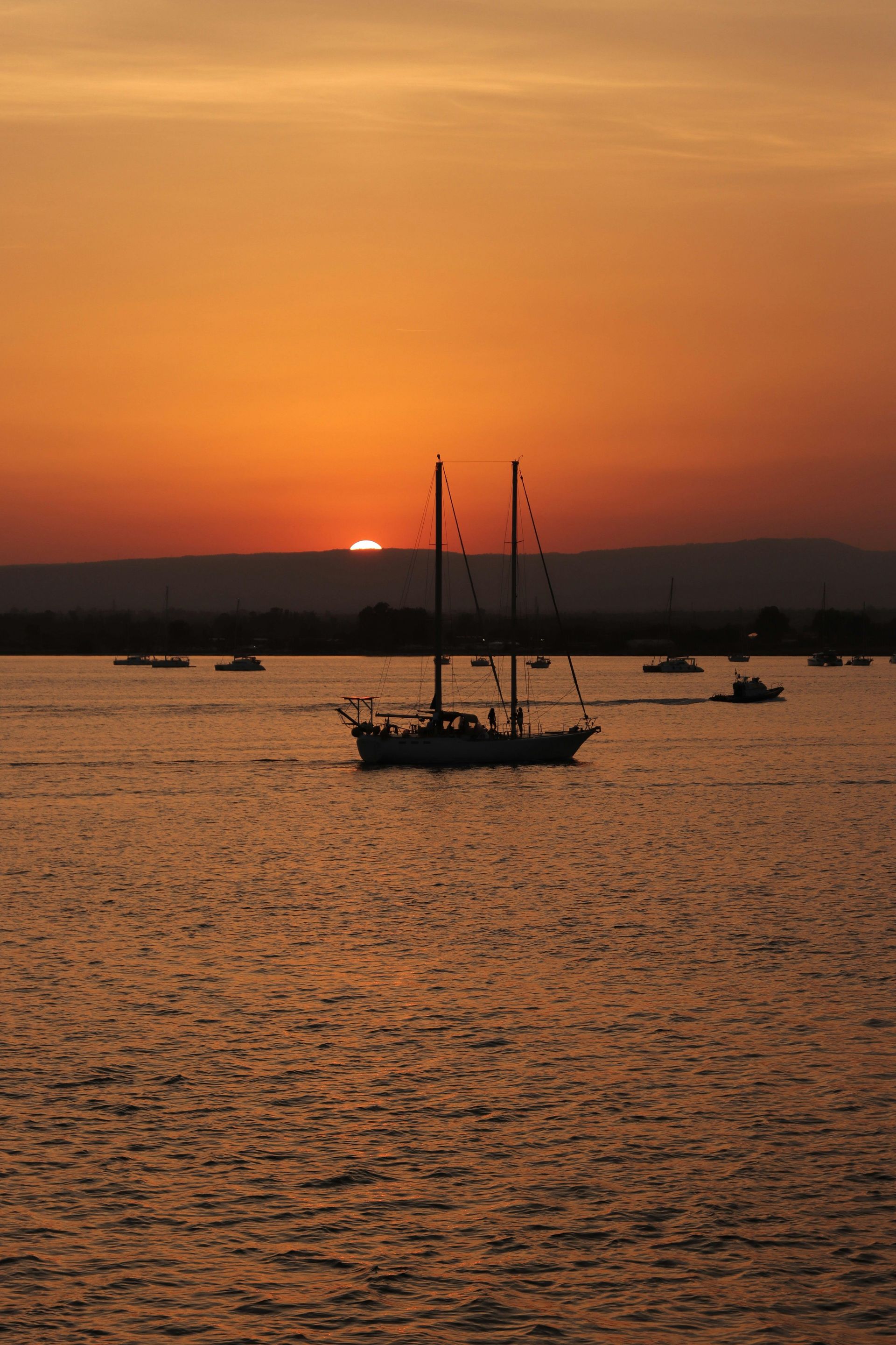 A sailboat is floating on top of a body of water at sunset in Sicily, Italy.