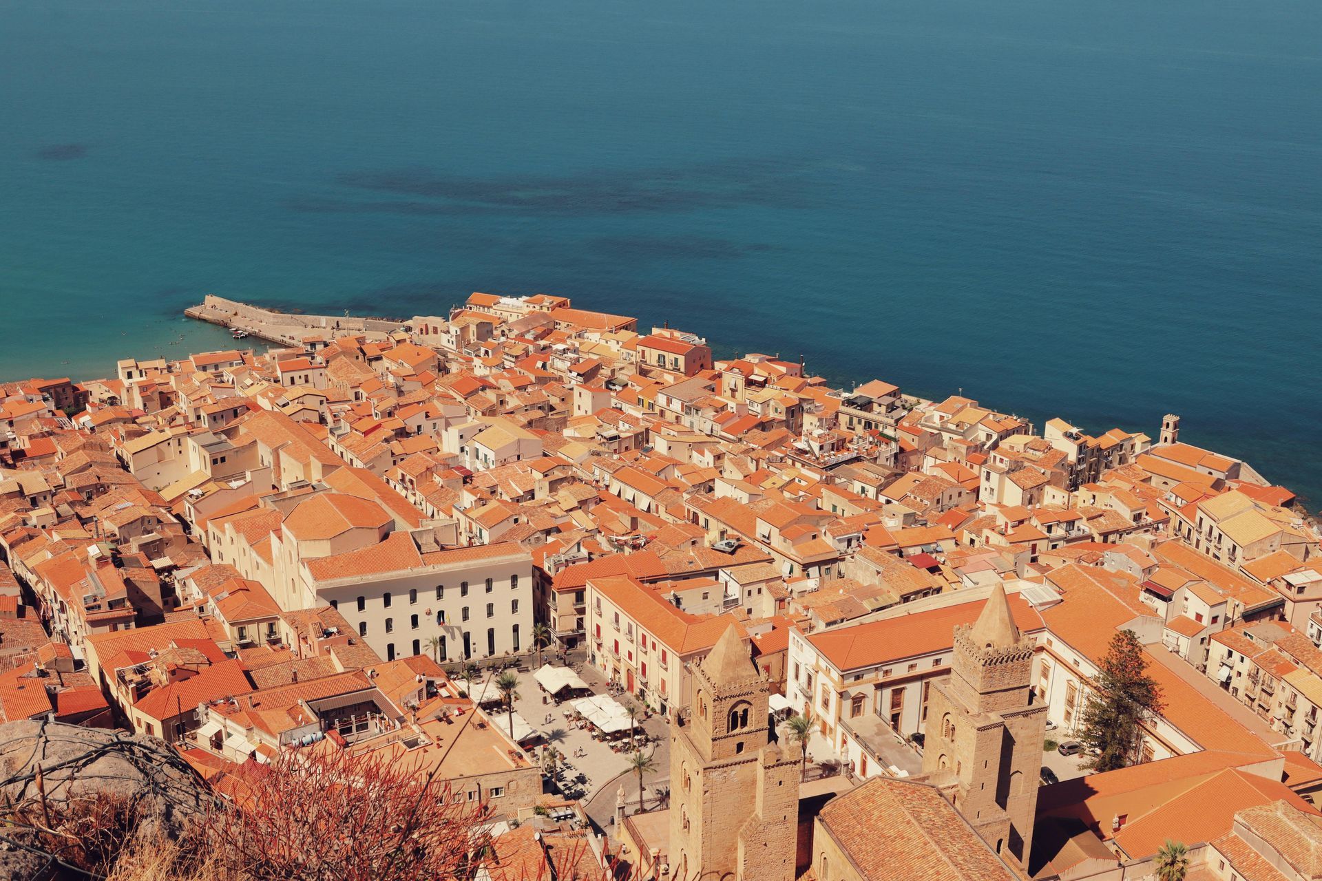 An aerial view of a city with red roofs next to the ocean in Sicily, Italy.