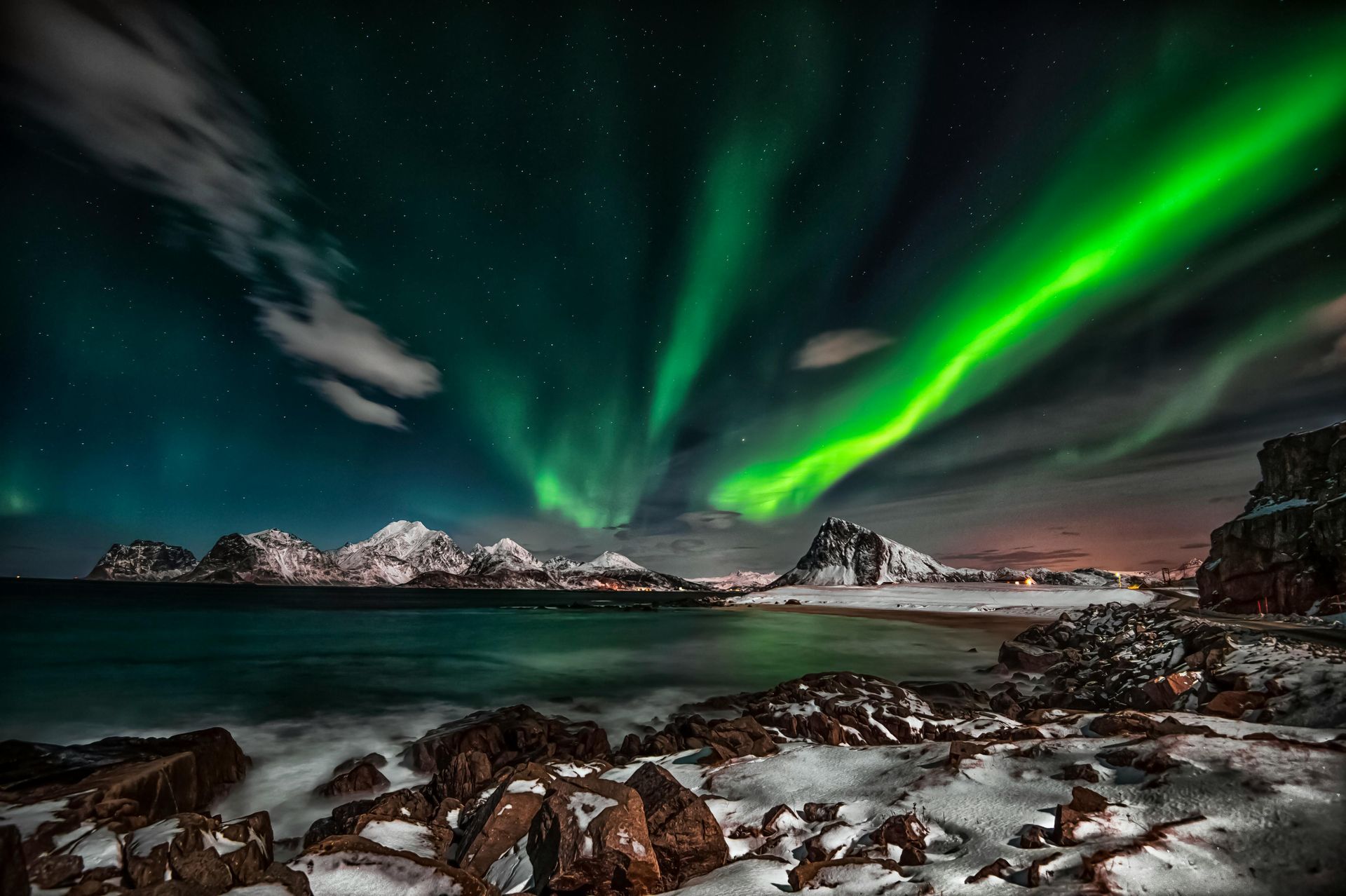 The aurora borealis is shining over the ocean and mountains on the Norwegian Coast.