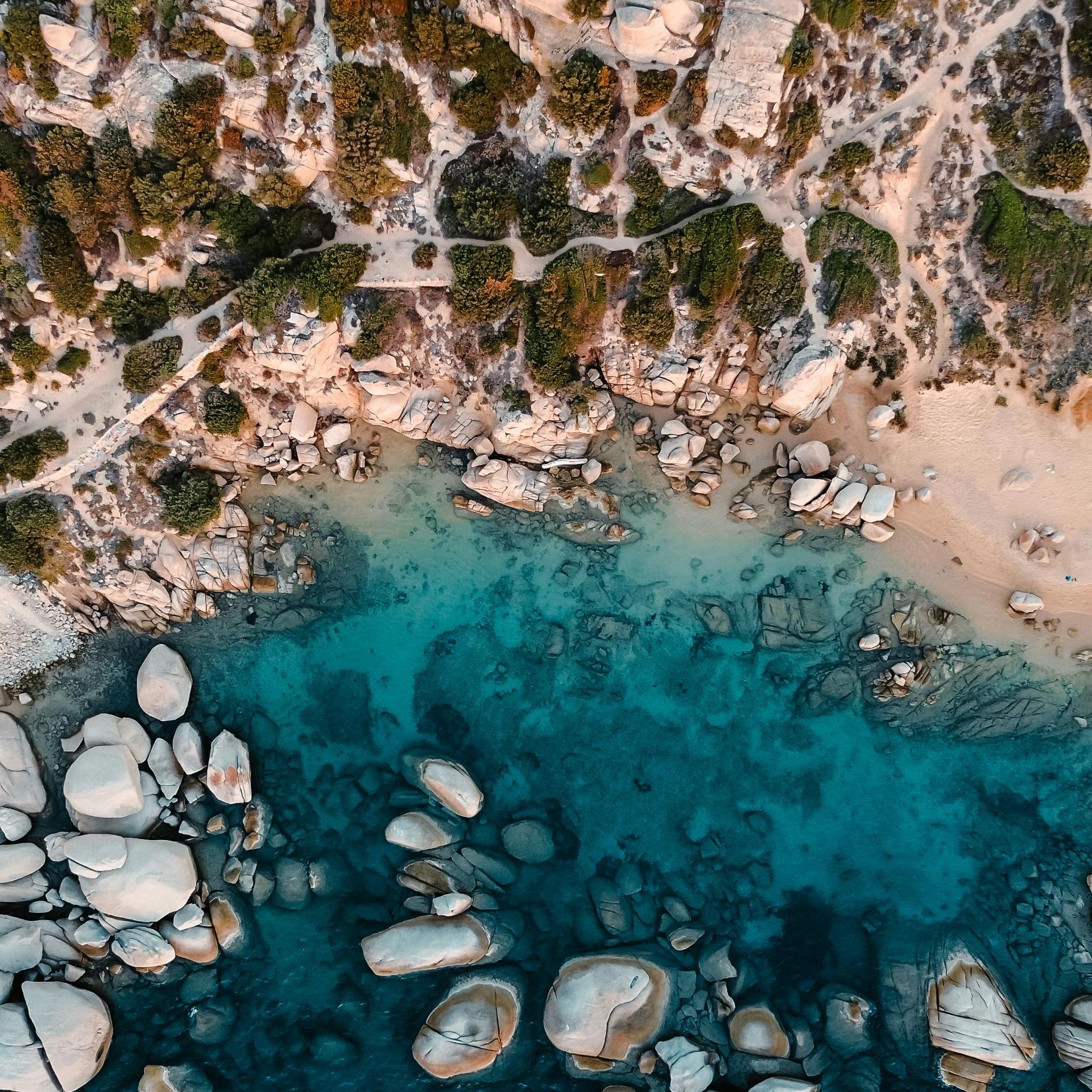 An aerial view of a beach with rocks and trees in Sardinia, Italy.