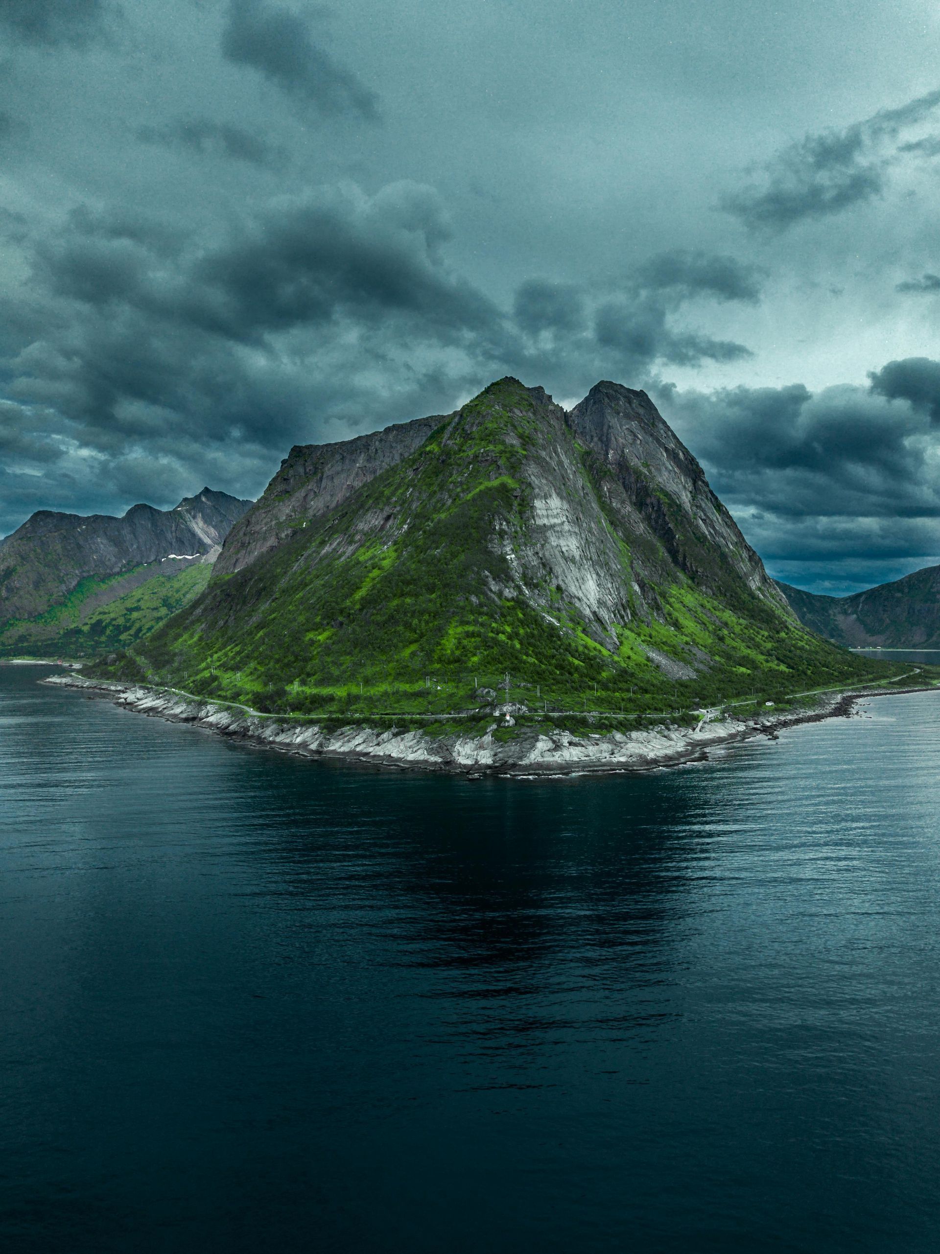 A small island in the middle of a body of water with mountains in the background on the Norwegian Coast.