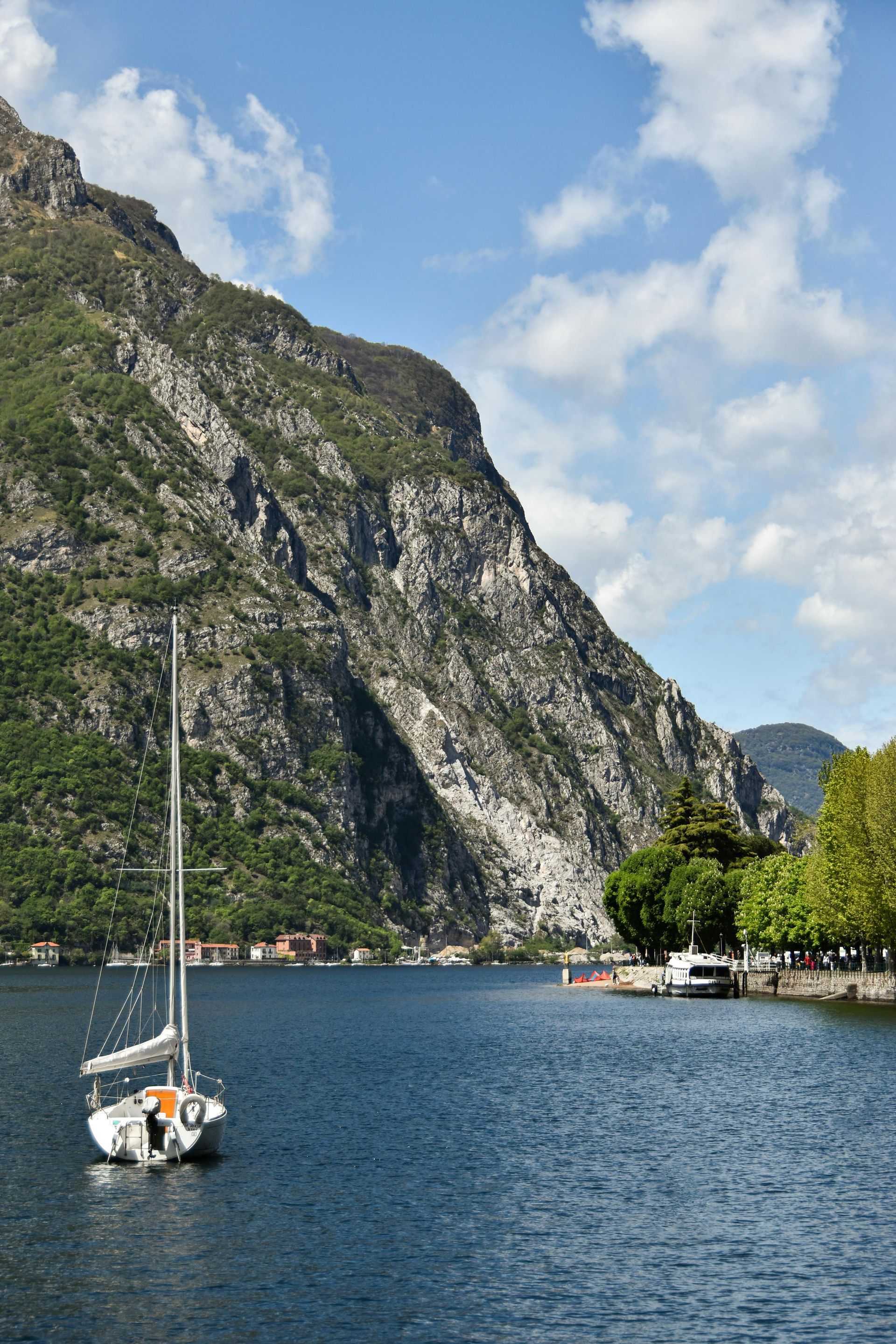 A sailboat is floating on Lake Como with mountains in the background in Italy.