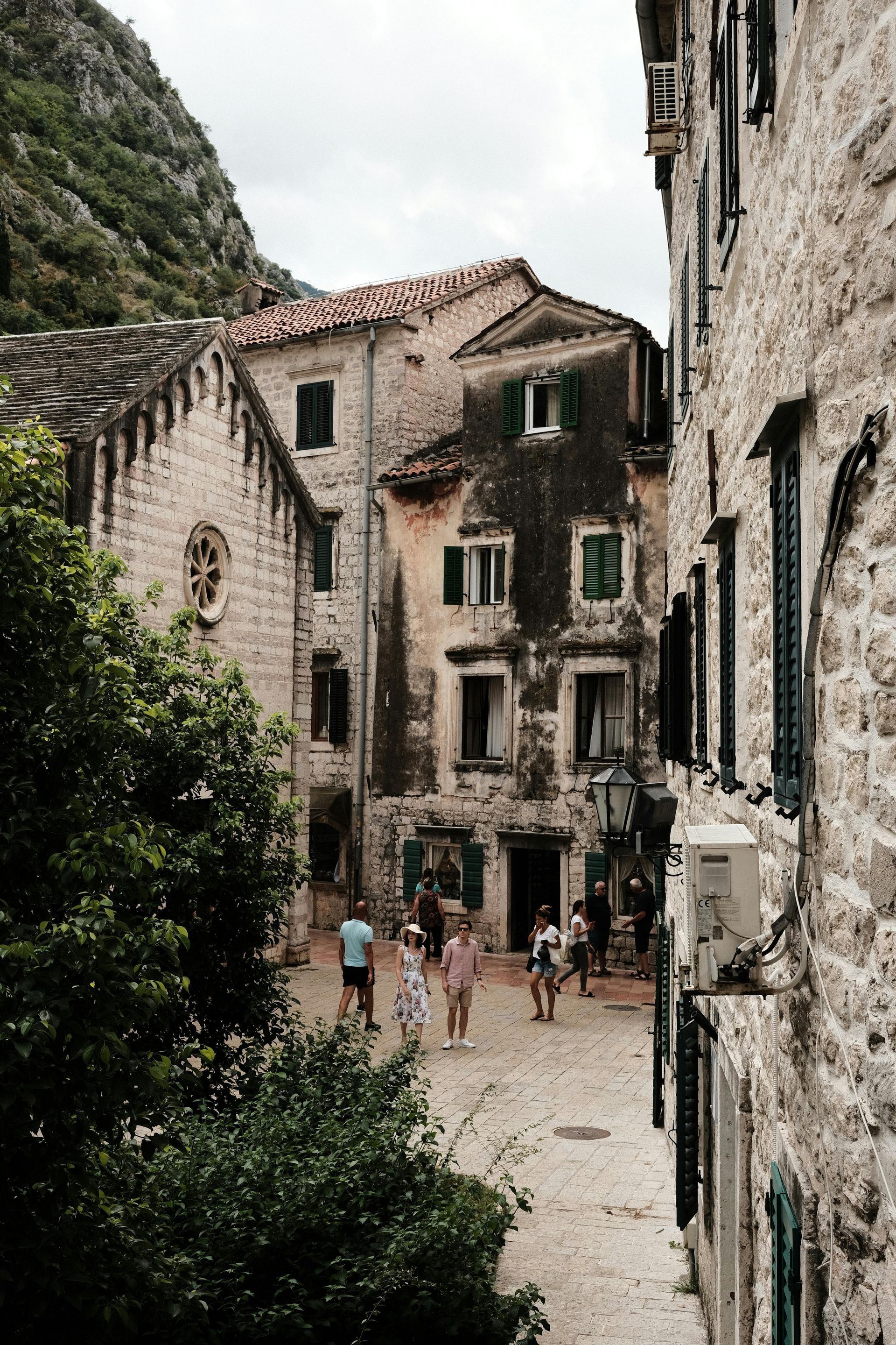 A group of people are walking down a narrow street between two stone buildings in Montenegro. 