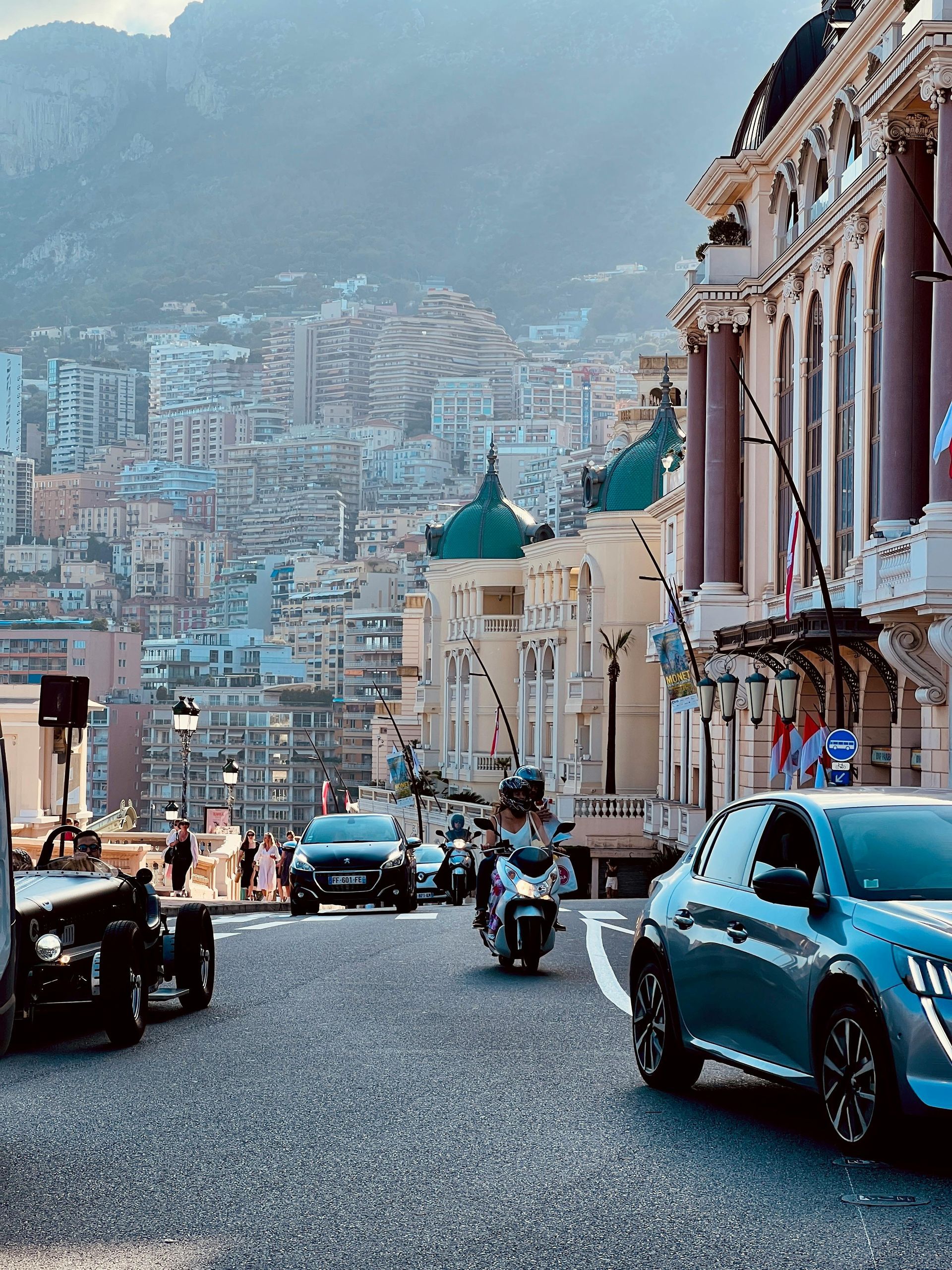 A group of cars and motorcycles are driving down a city street in Monaco.