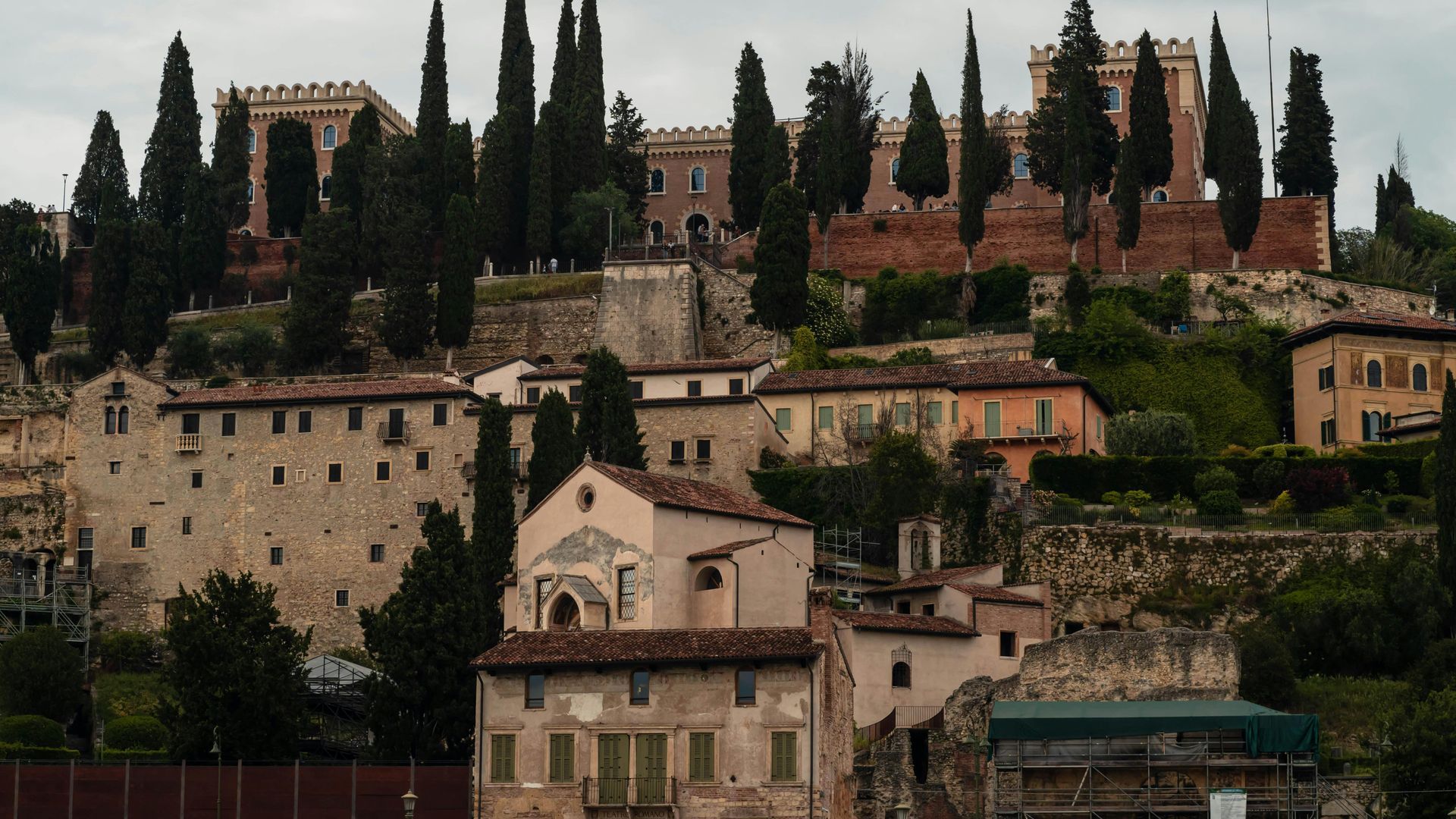 A castle sits on top of a hill surrounded by trees and buildings in Verona, Italy.