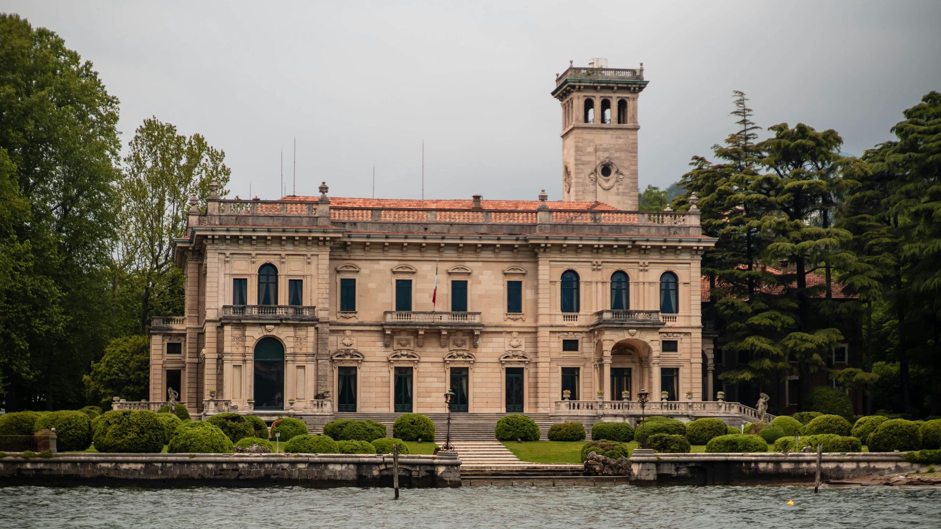 A large building with a clock tower is next to Lake Como in Italy.