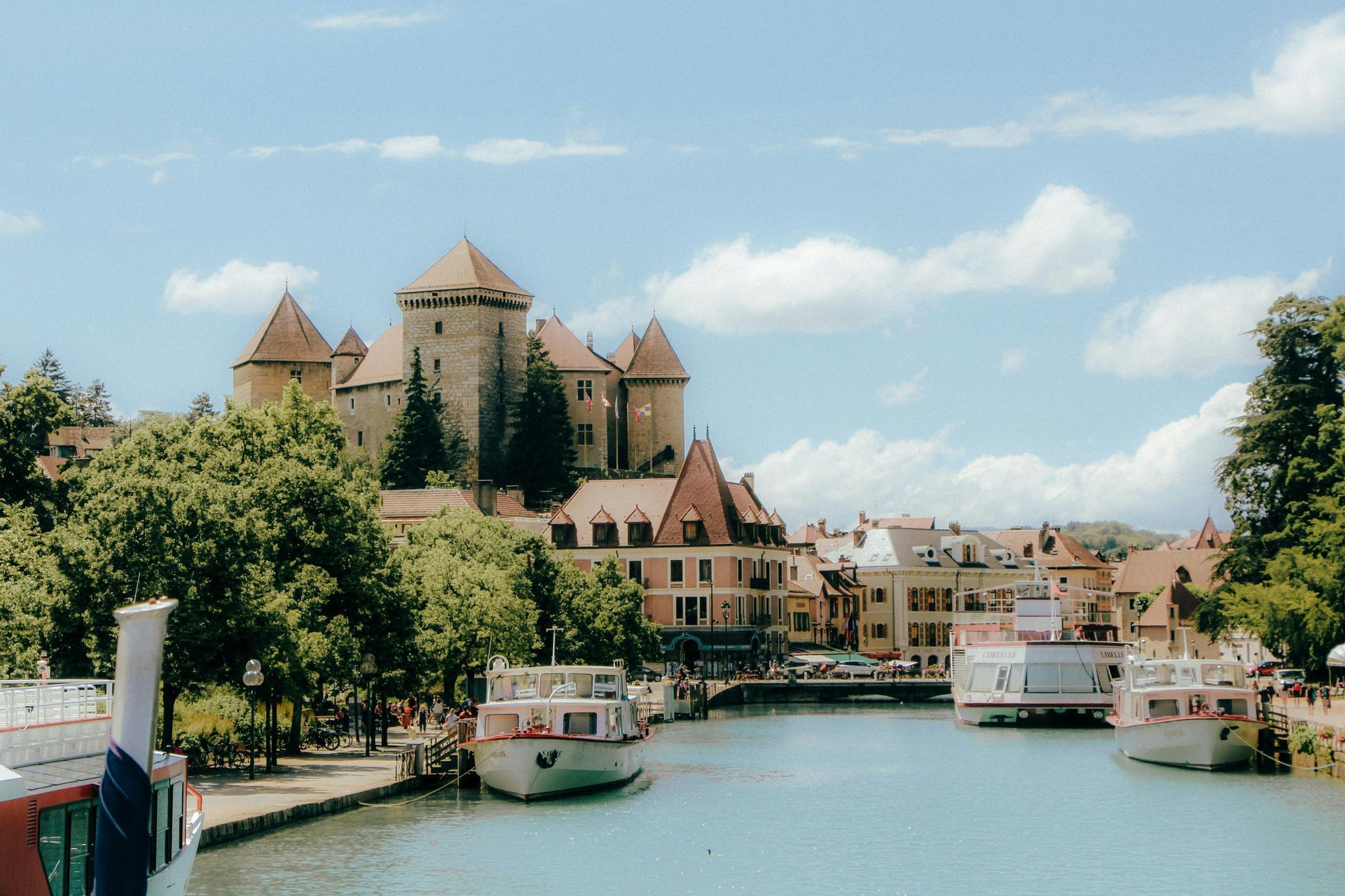 A river with a castle in the background and boats in the foreground in Annecy, France.