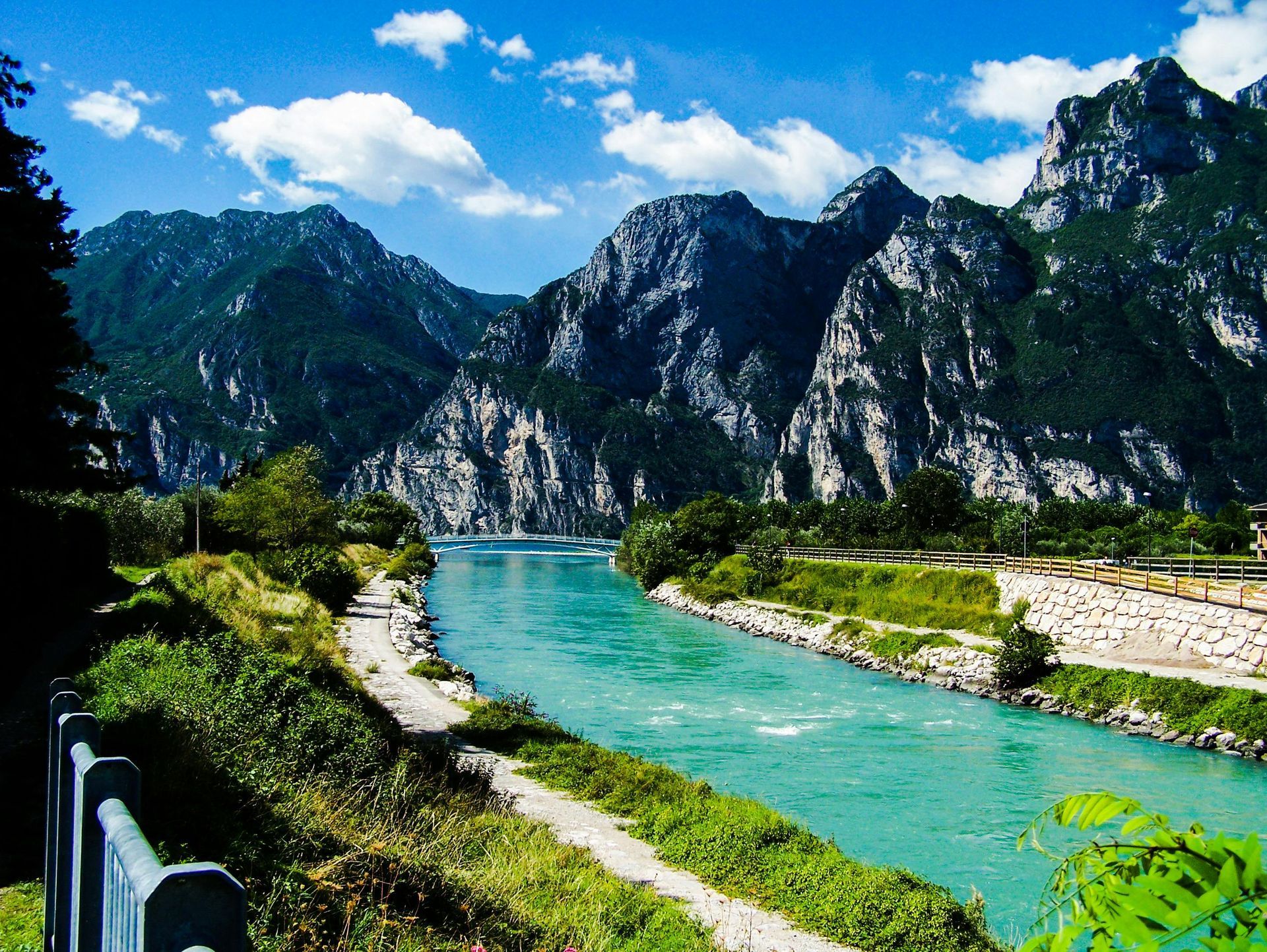 A river with mountains in the background and a fence in the foreground near Lake Garda, Italy.