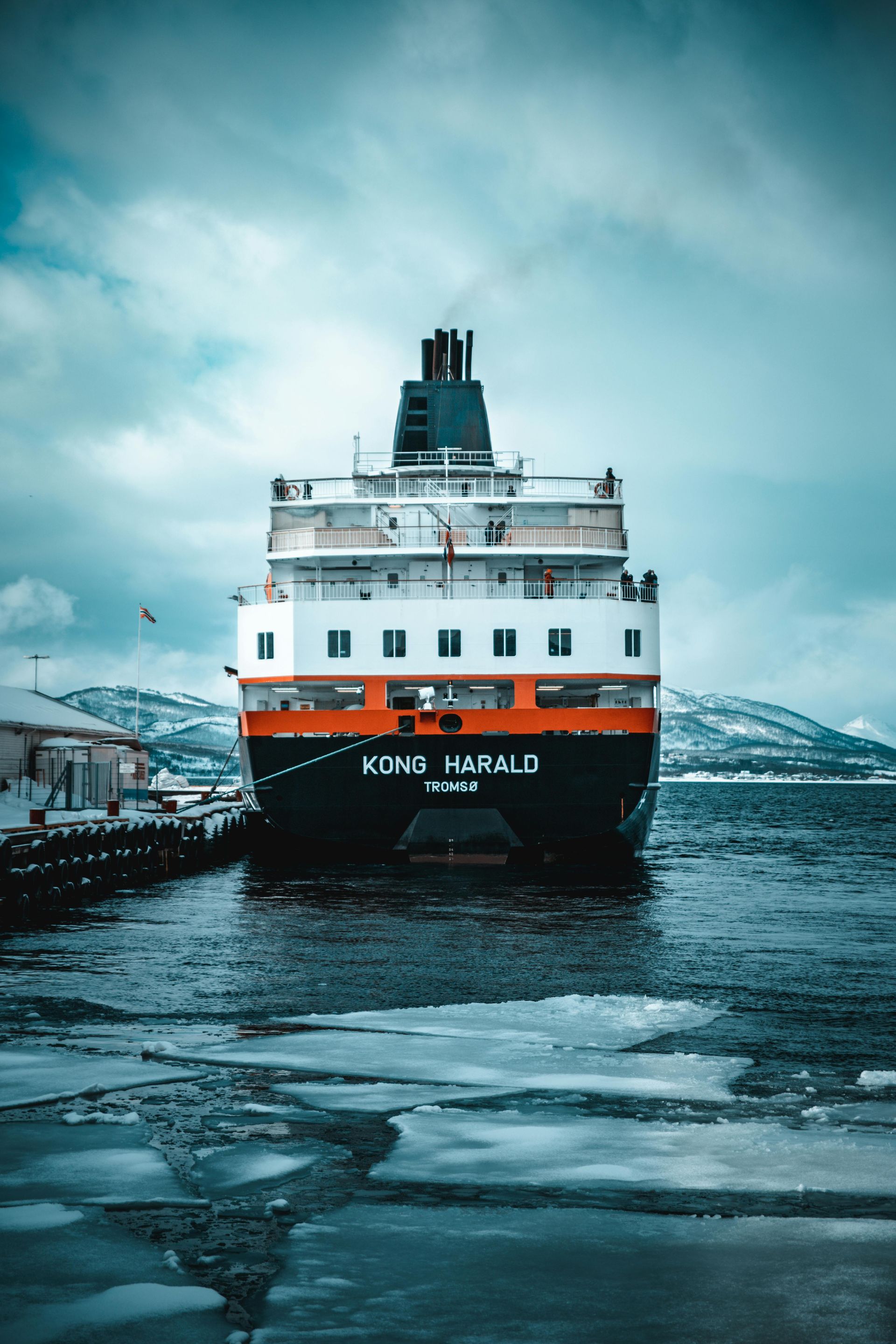 A large cruise ship is docked in a body of water  on the Norwegian Coast.