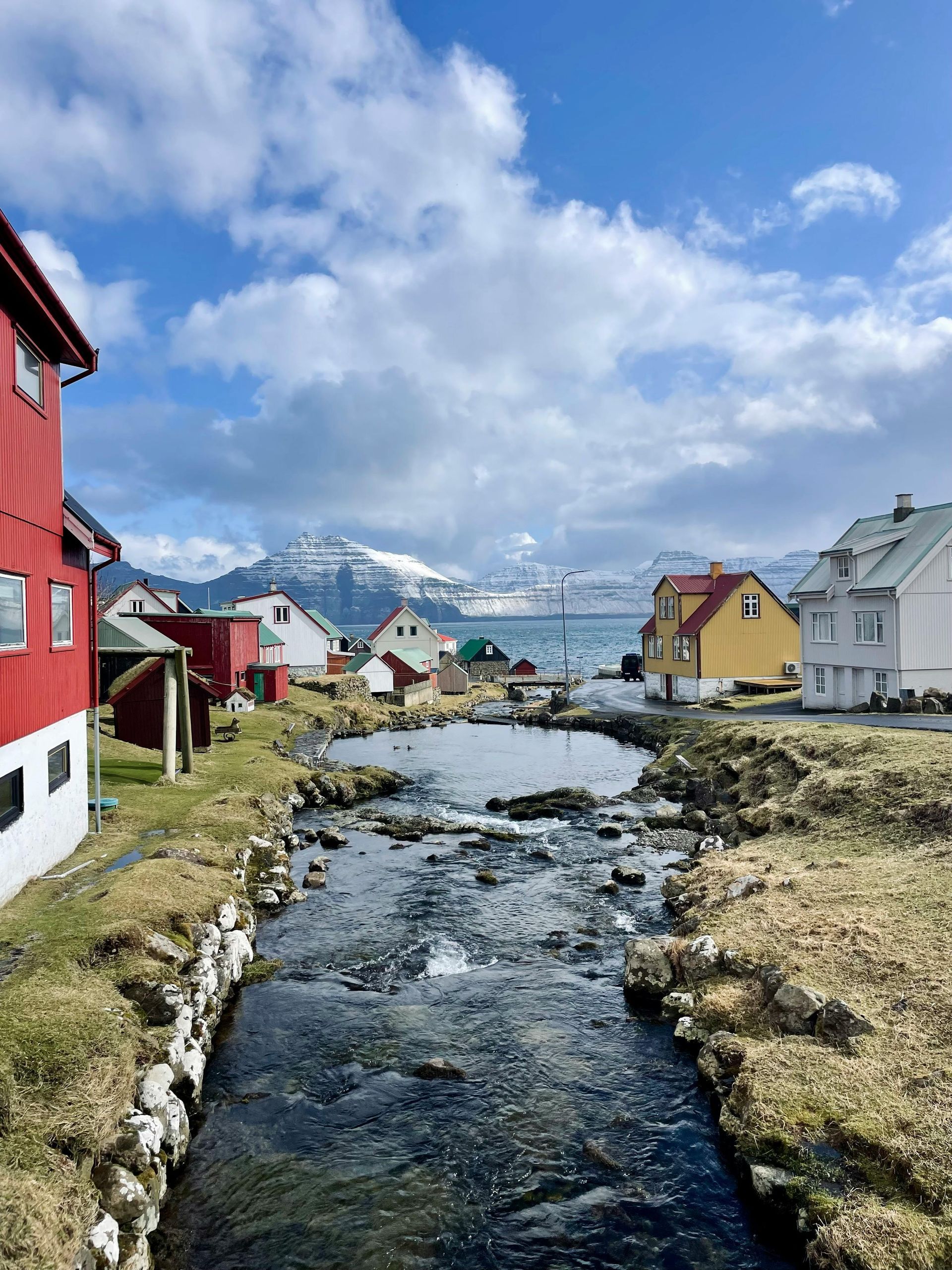 A river running through a small village with houses and mountains in the background on the Faroe Islands.