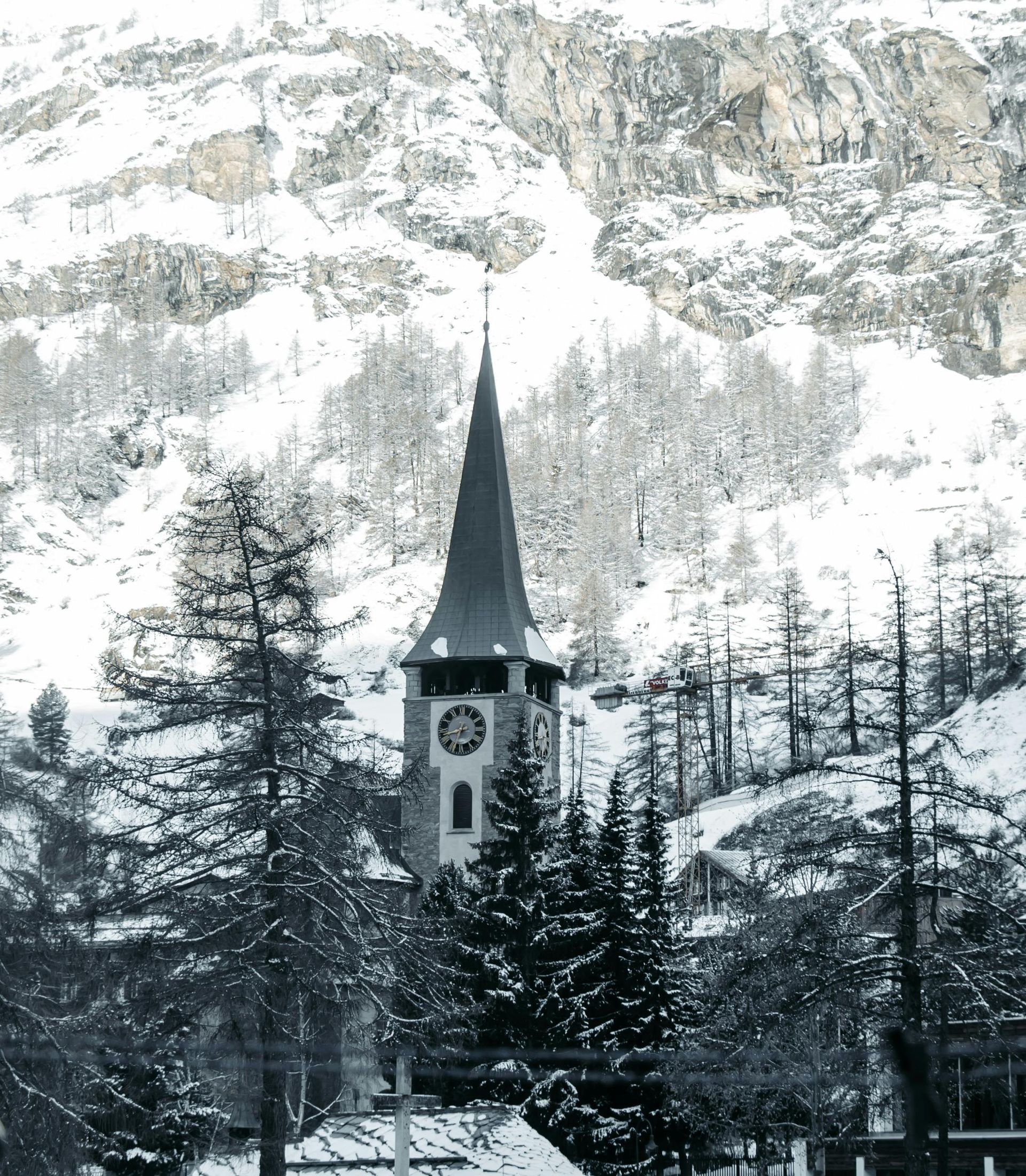 A clock tower in the middle of a snowy forest in Switzerland.