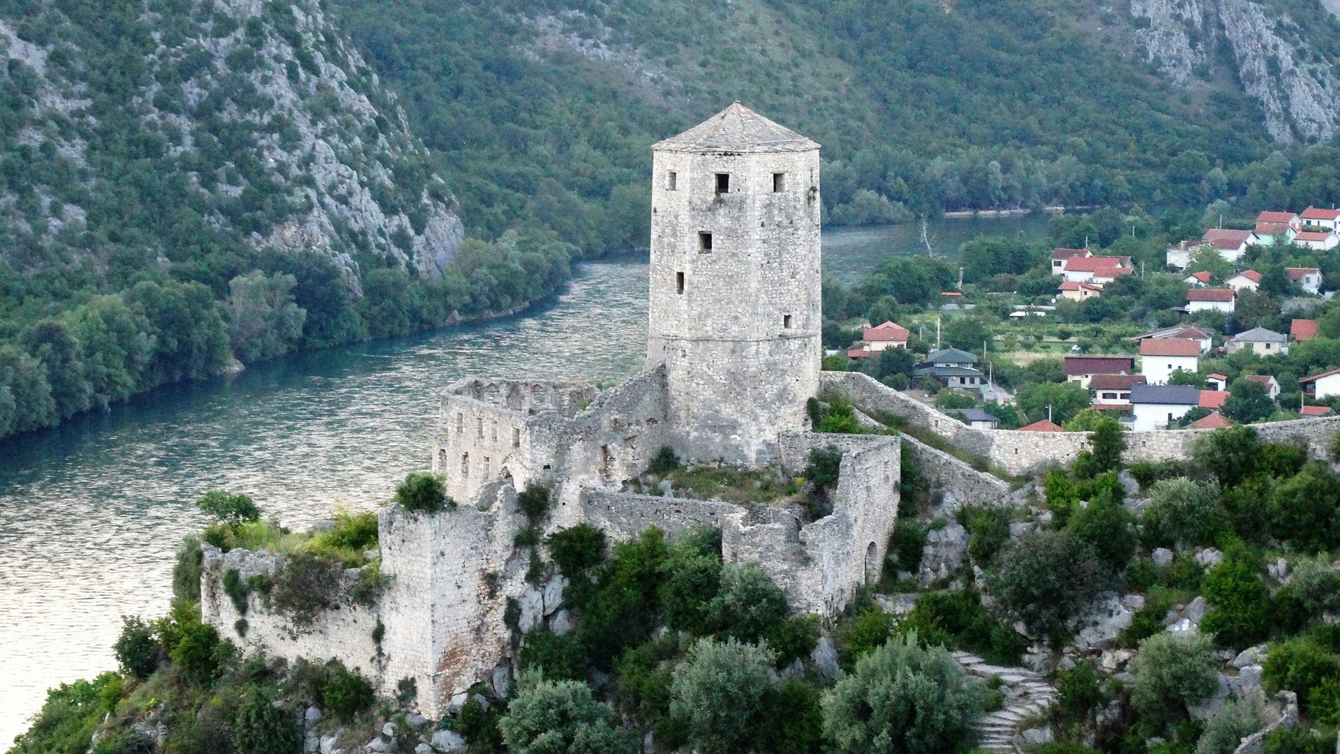 A castle is sitting on top of a hill next to a river in Mostar, Bosnia and Herzegovina.