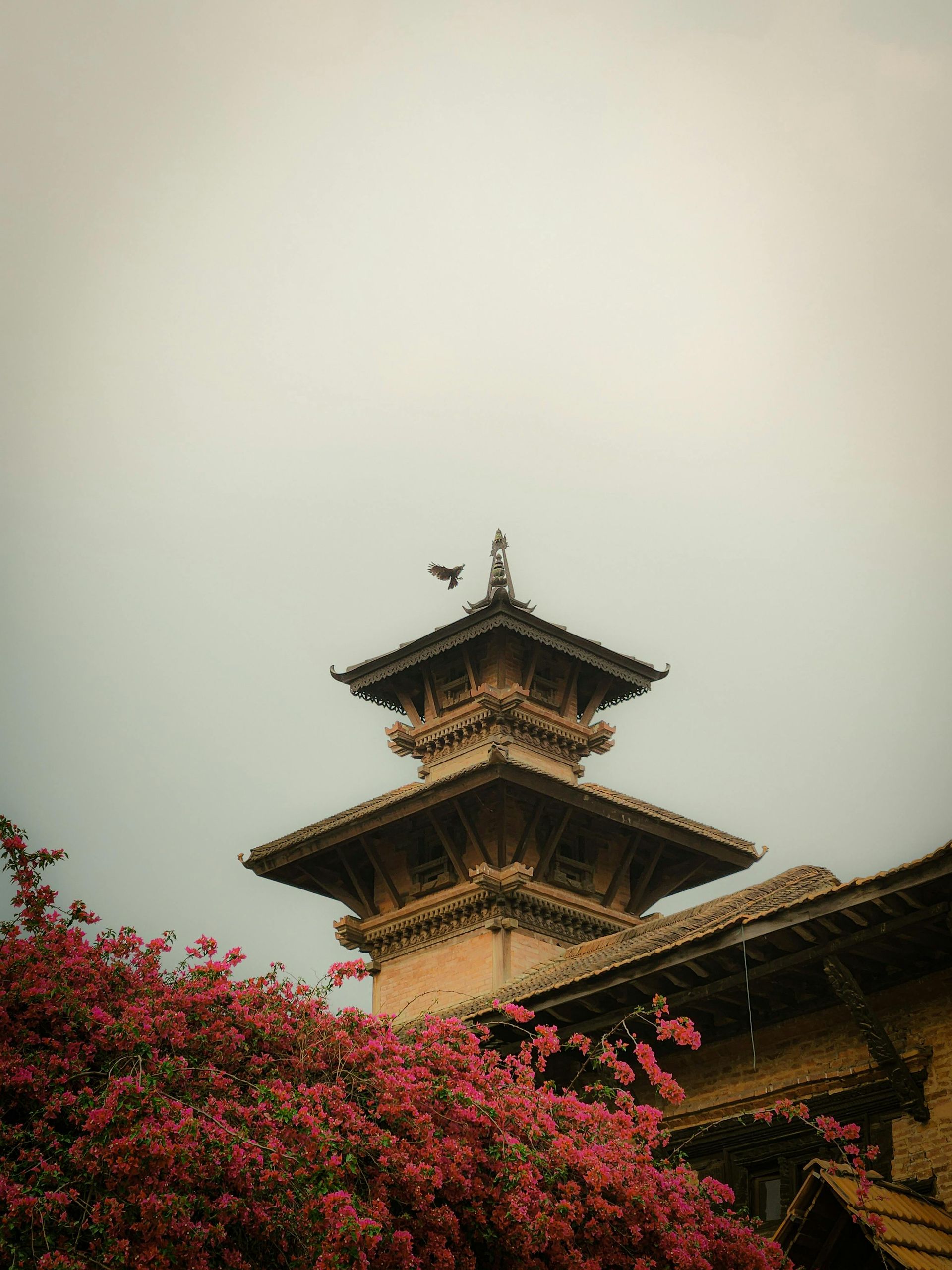 A tower with a bird on top of it is surrounded by pink flowers  in Bhutan.