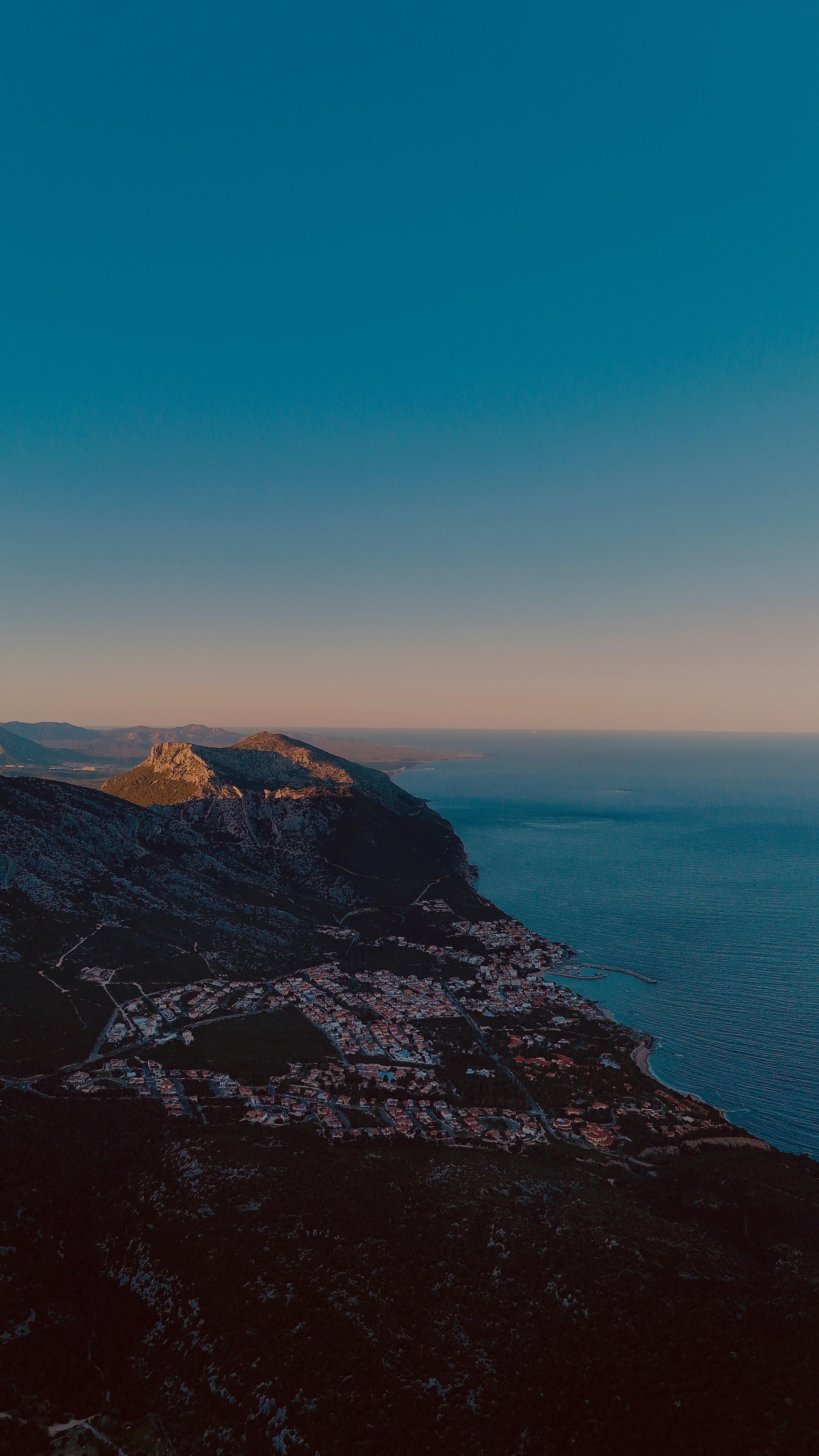 An aerial view of a cliff overlooking the ocean at sunset in Sardinia, Italy.