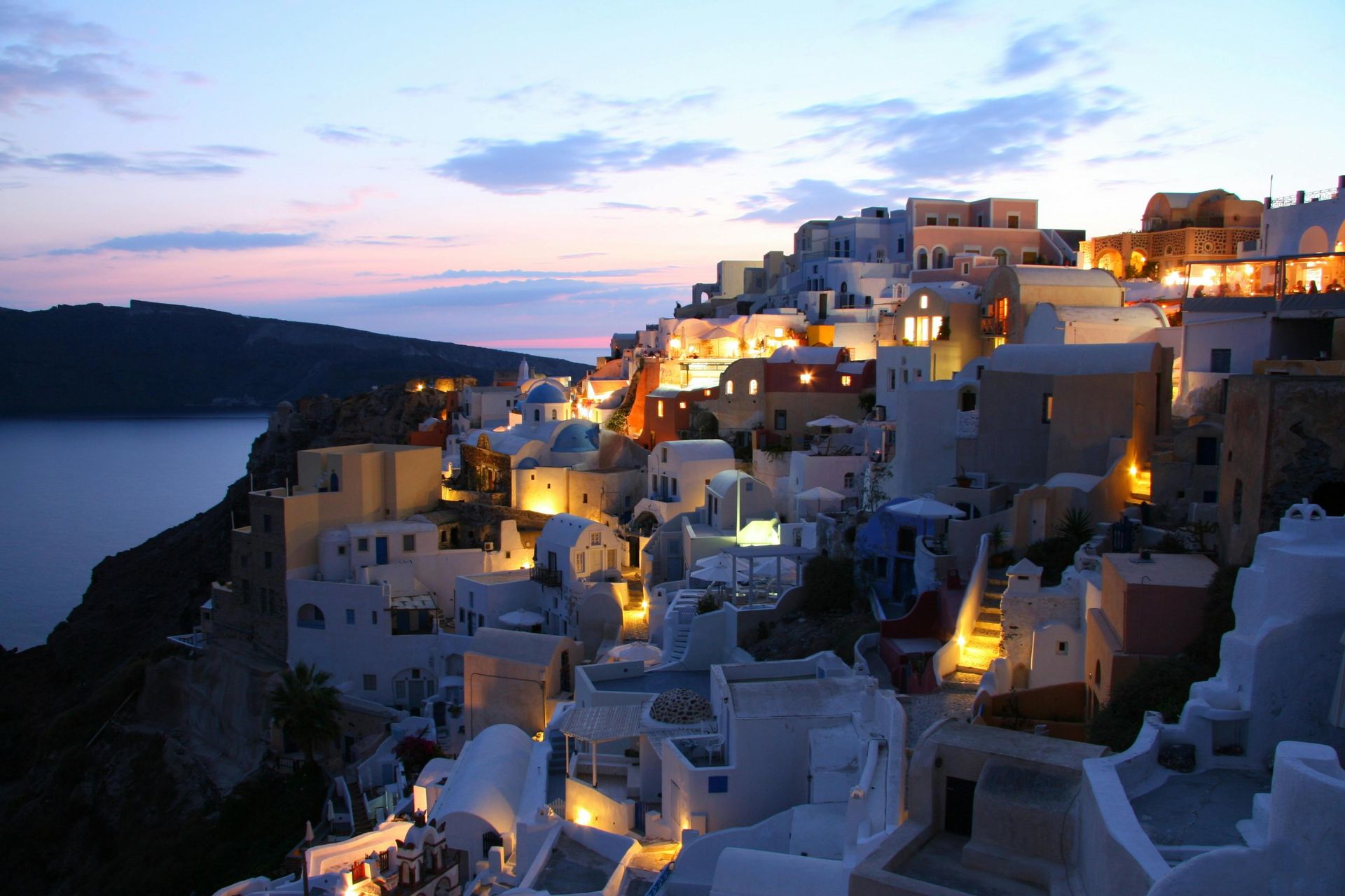 The buildings are lit up at night and there is a body of water in the background in Santorini, Greece.