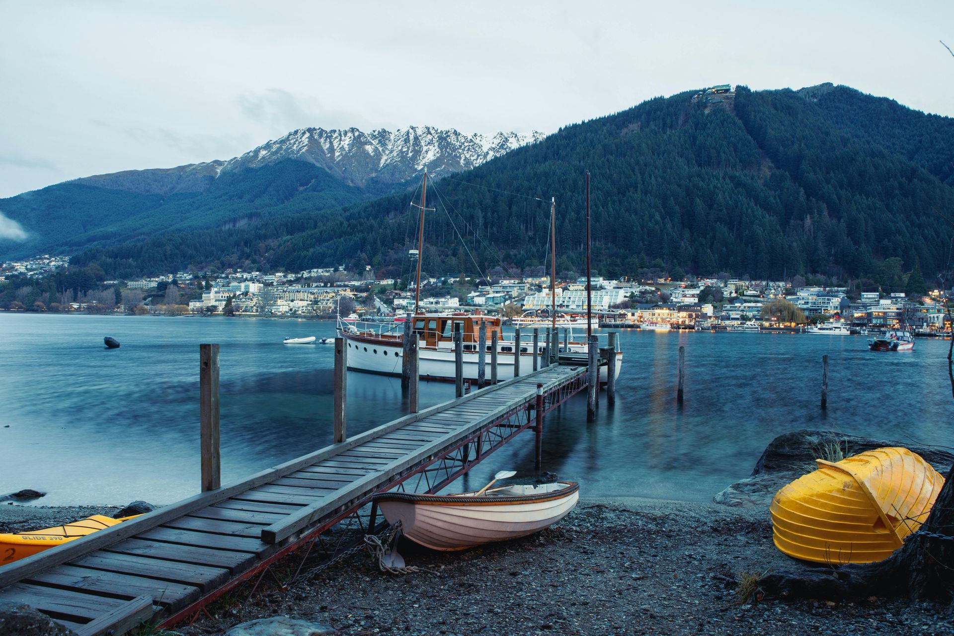 A dock with boats docked on it and mountains in the background in New Zealand.