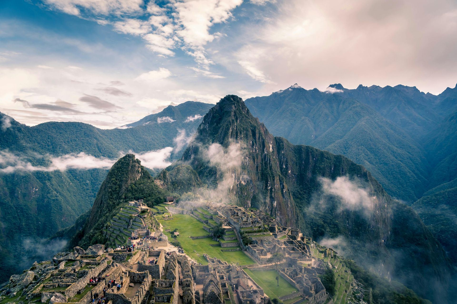 An aerial view of the ruins of Machu Picchu surrounded by mountains and clouds in Peru.