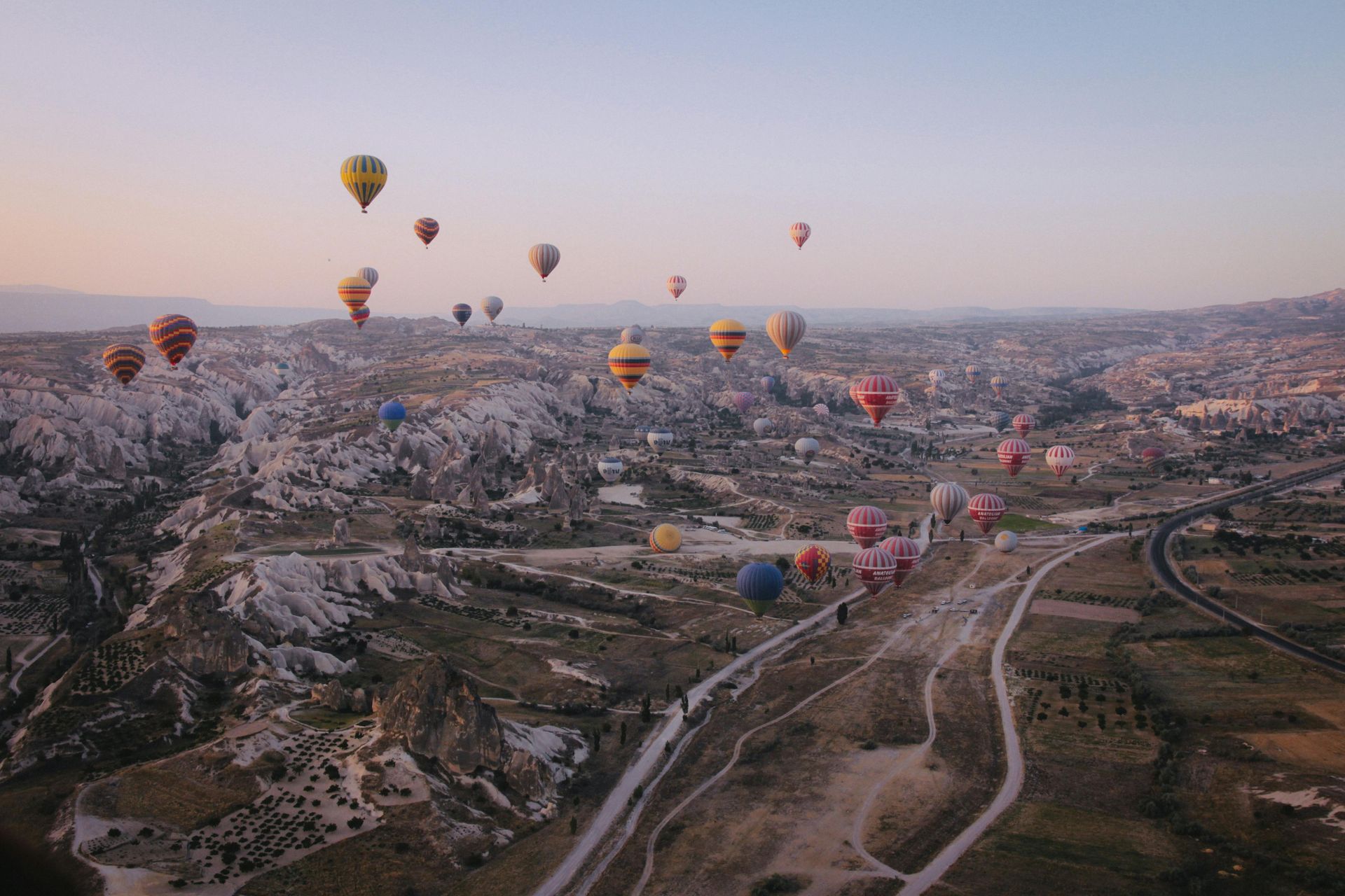 A bunch of hot air balloons are flying over a valley in Cappadocia, Turkey. 