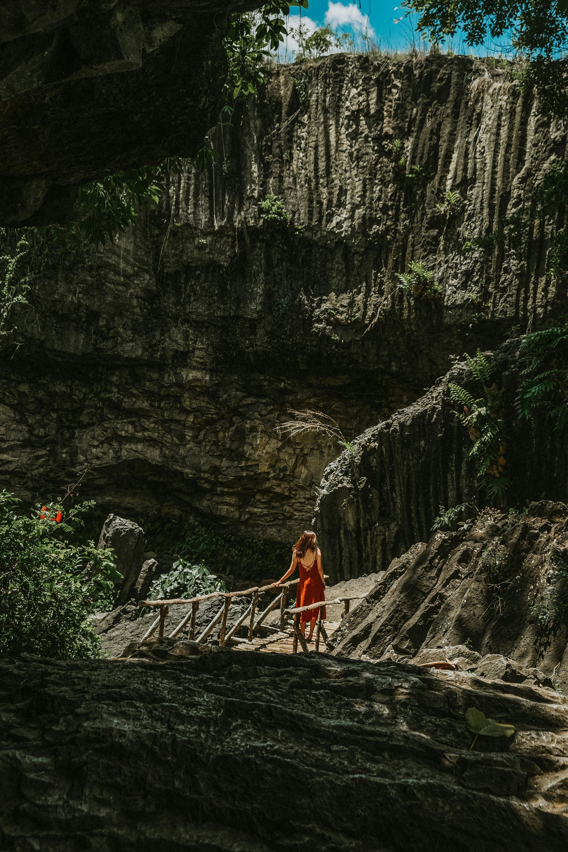 A woman in a red dress is standing on a rocky cliff in Vietnam.