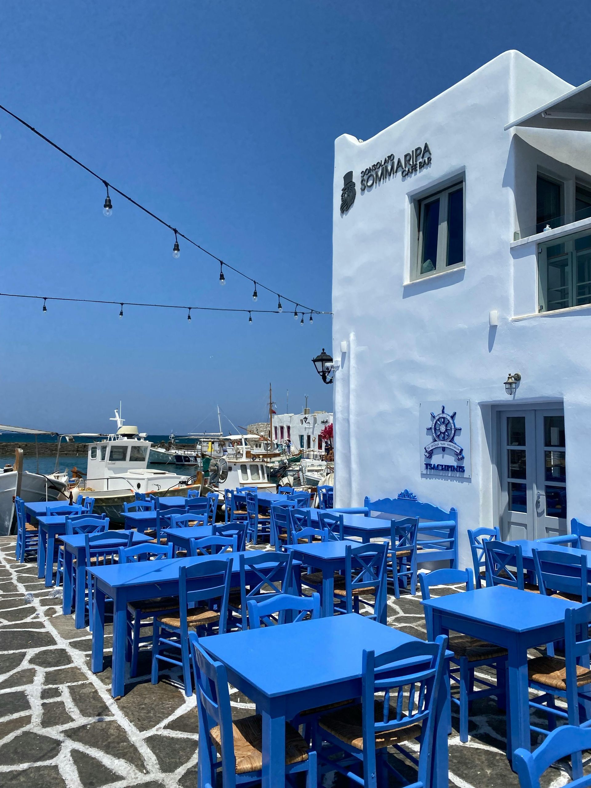 A white building with blue tables and chairs in front of it in Paros, Greece.