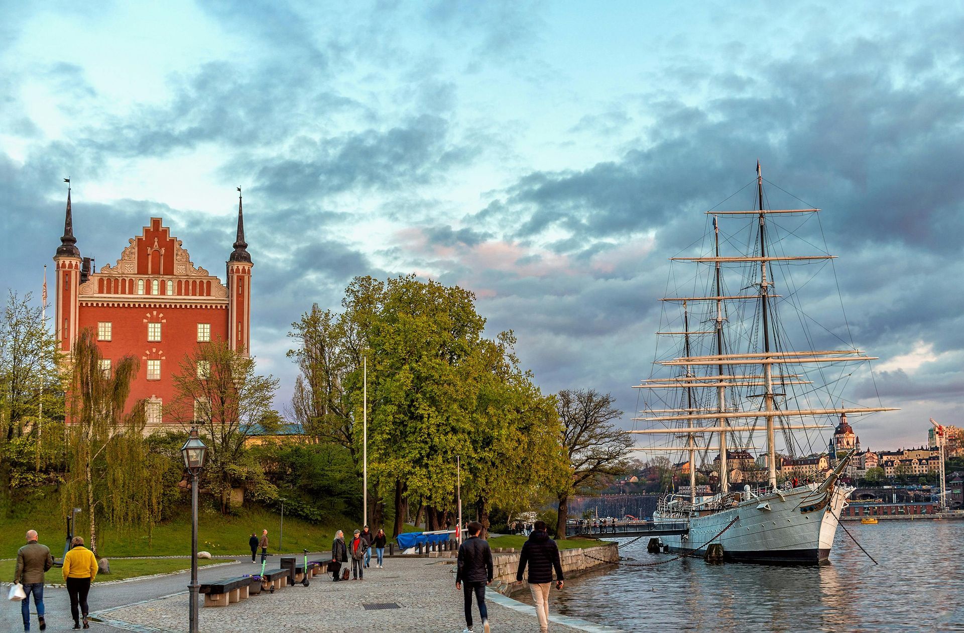 A group of people are walking along a sidewalk next to a body of water in Sweden.