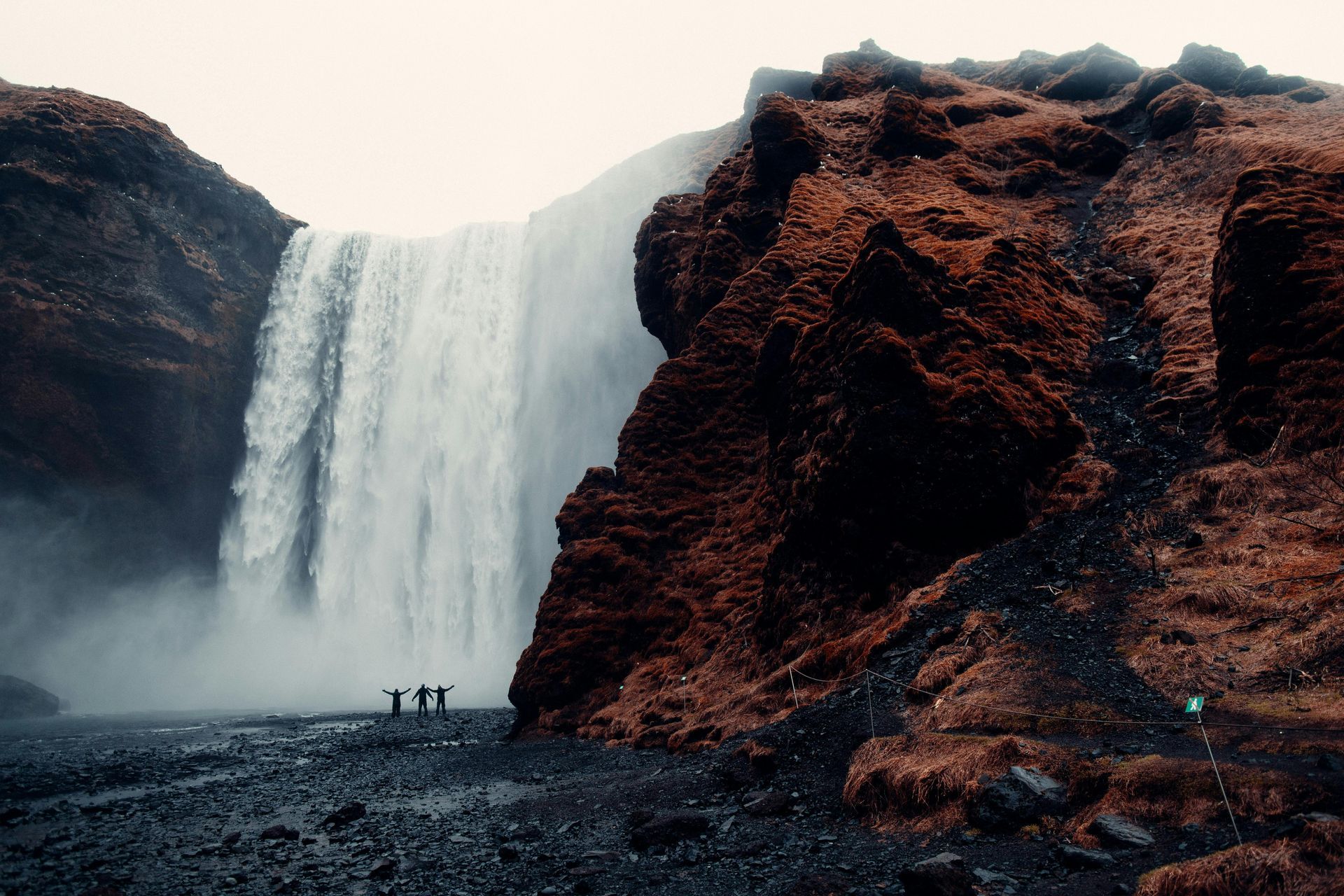 A waterfall is surrounded by rocks and people are standing in front of it in Iceland.