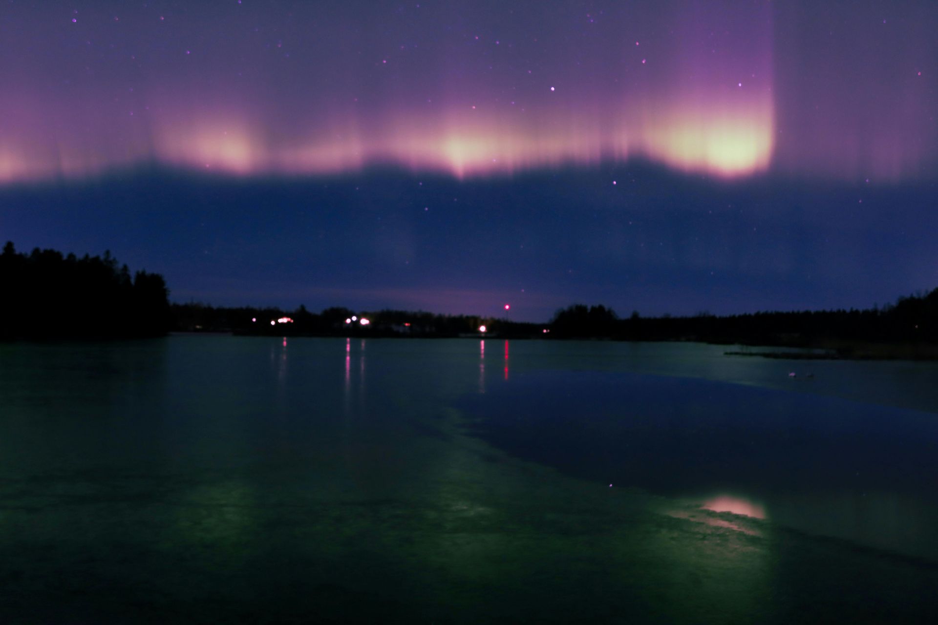 The aurora borealis is shining over a lake at night in Sweden.