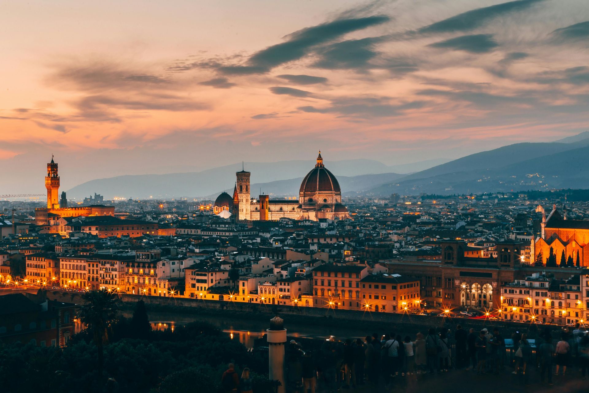 An aerial view of Florence, Italy at night with a sunset in the background.