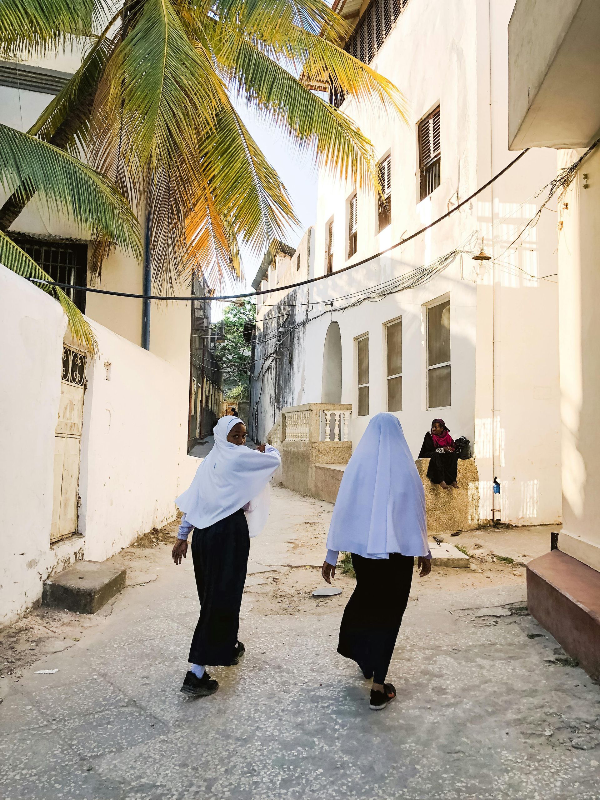 Two women are walking down a street in front of a white building in Tanzania, Africa.