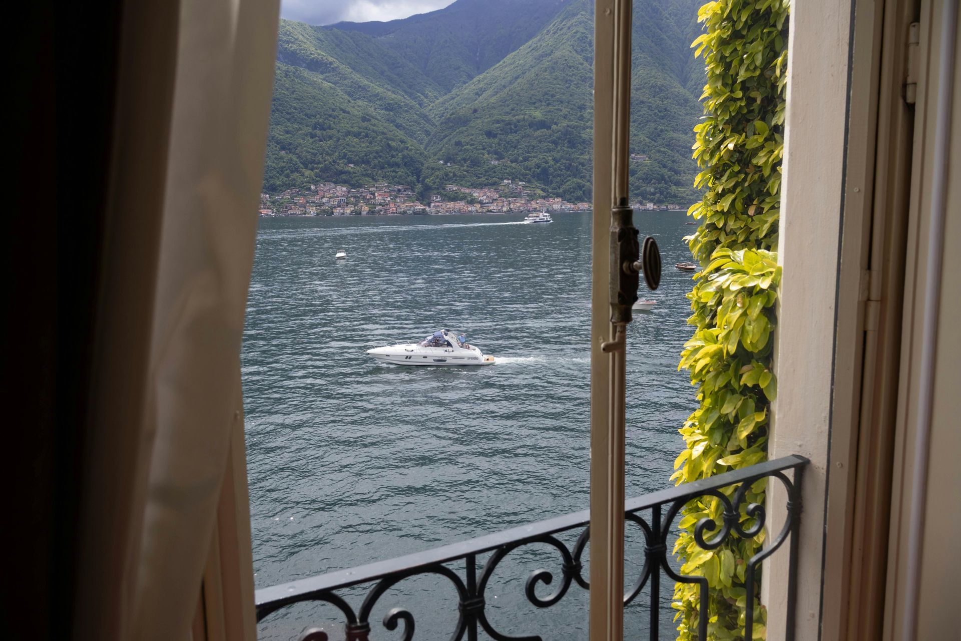 A view of Lake Como from a window with a boat in the water in Italy.