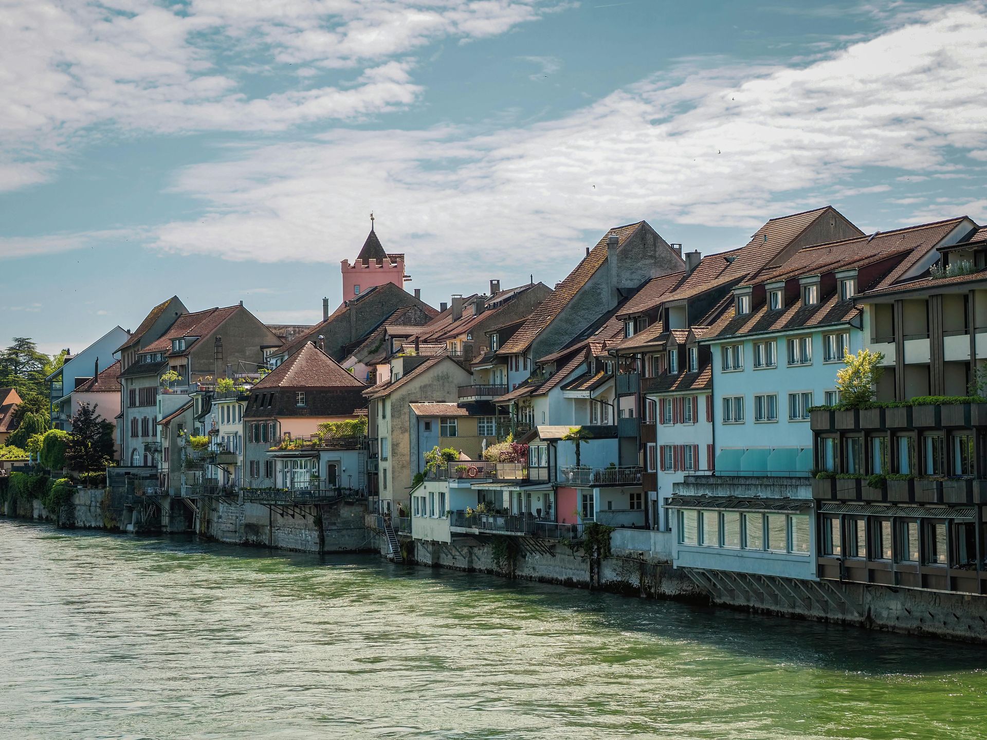 A row of buildings along The Rhine River with a castle in the background.