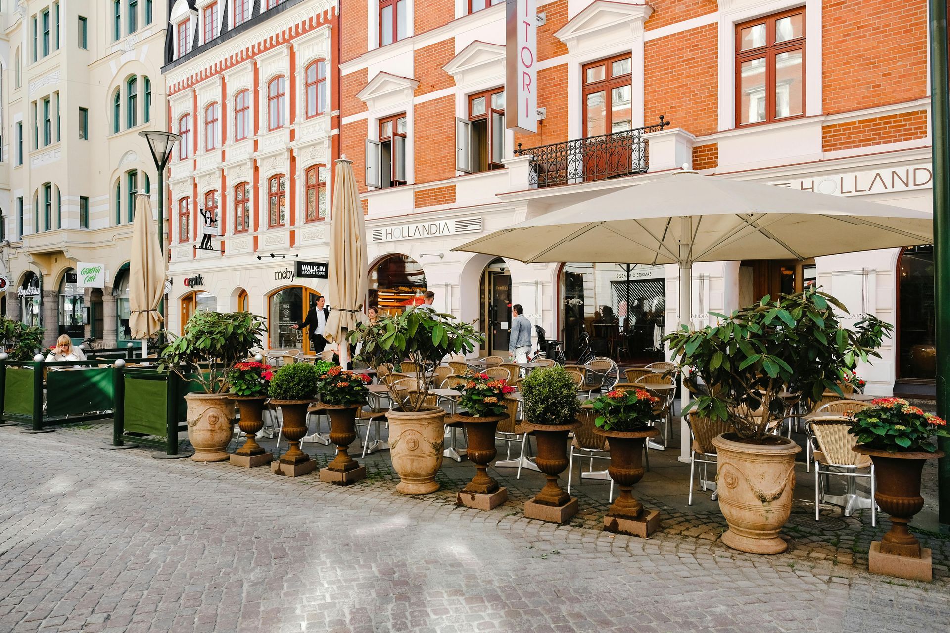 A restaurant with umbrellas and potted plants in front of a brick building in Sweden.