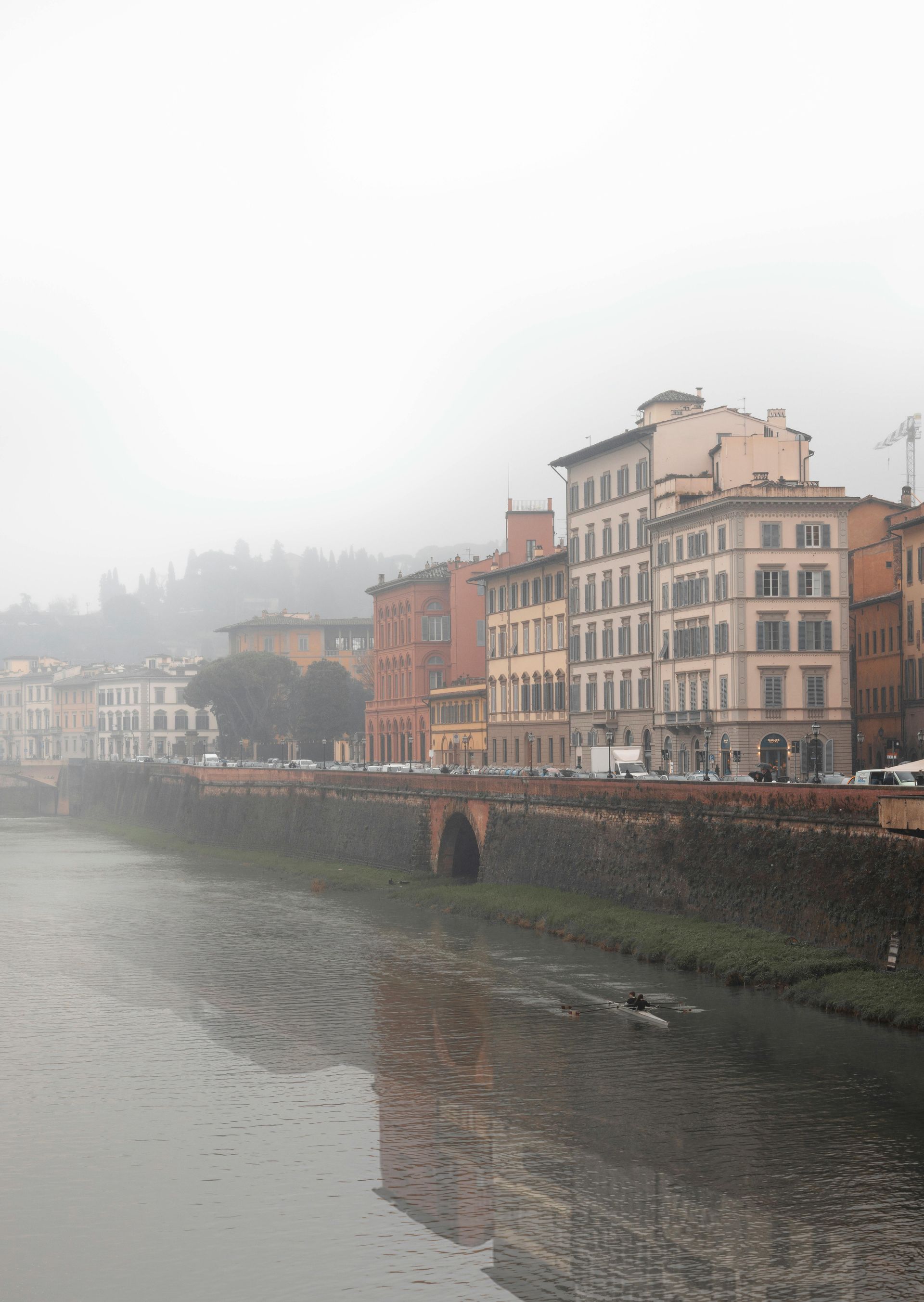 A river surrounded by buildings on a foggy day in Florence, Italy.