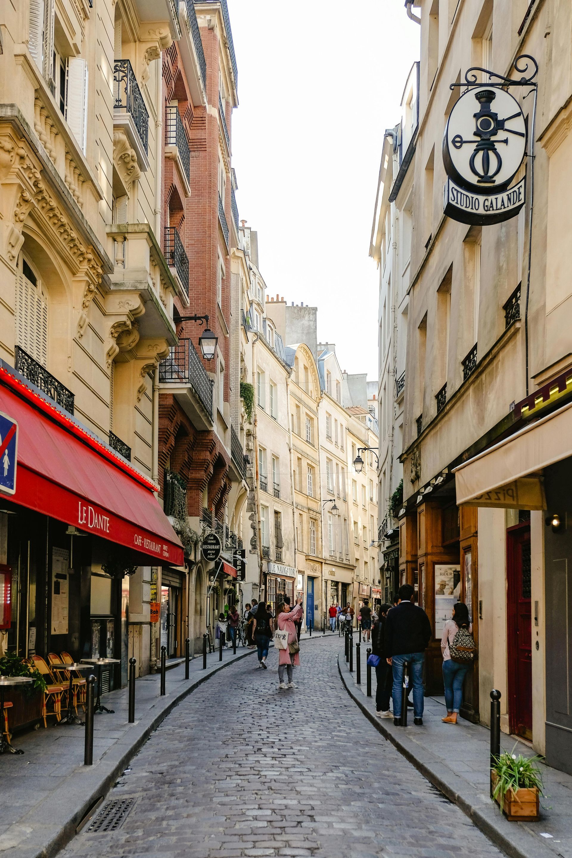 A narrow cobblestone street in paris between two buildings with people walking down it.