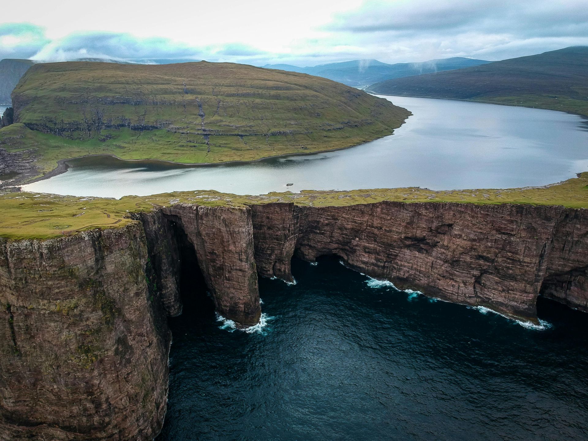 An aerial view of a mountain cliff overlooking a body of water on the Faroe Islands.