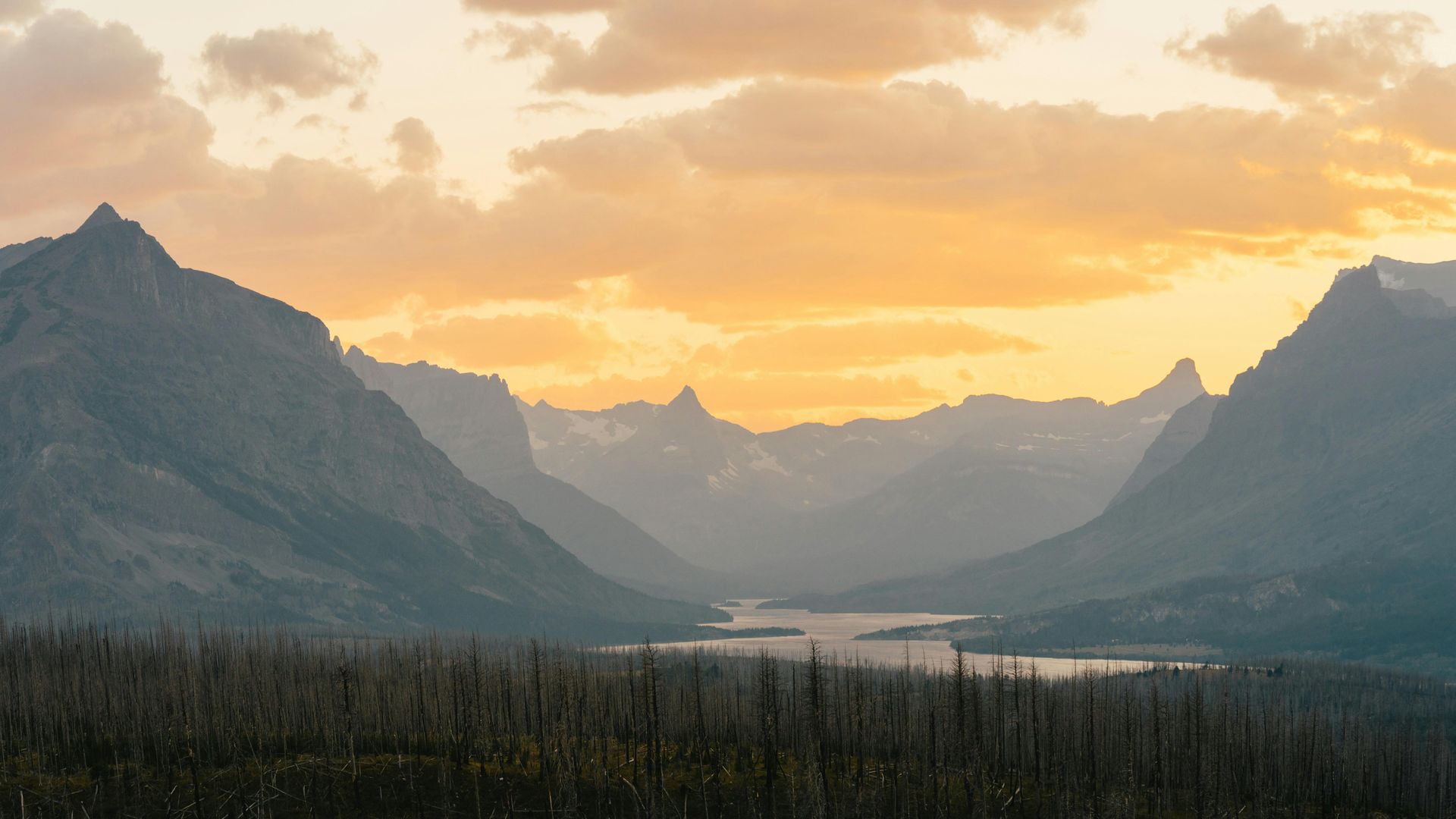 A sunset over a mountain range with a lake in the middle at Glacier National Park in Montana. 