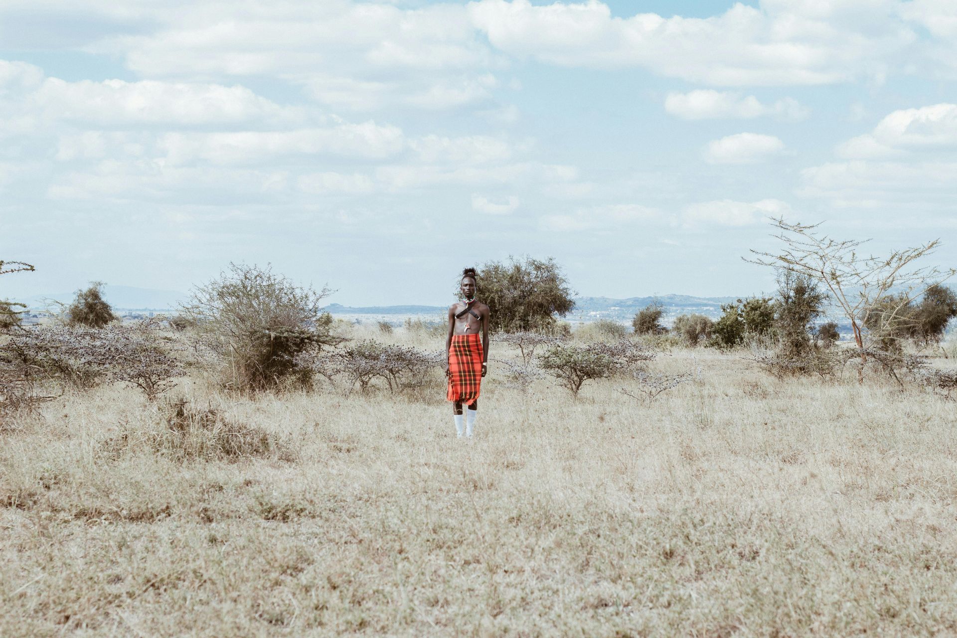 A man in a red dress is walking through a dry grass field in Kenya Africa.