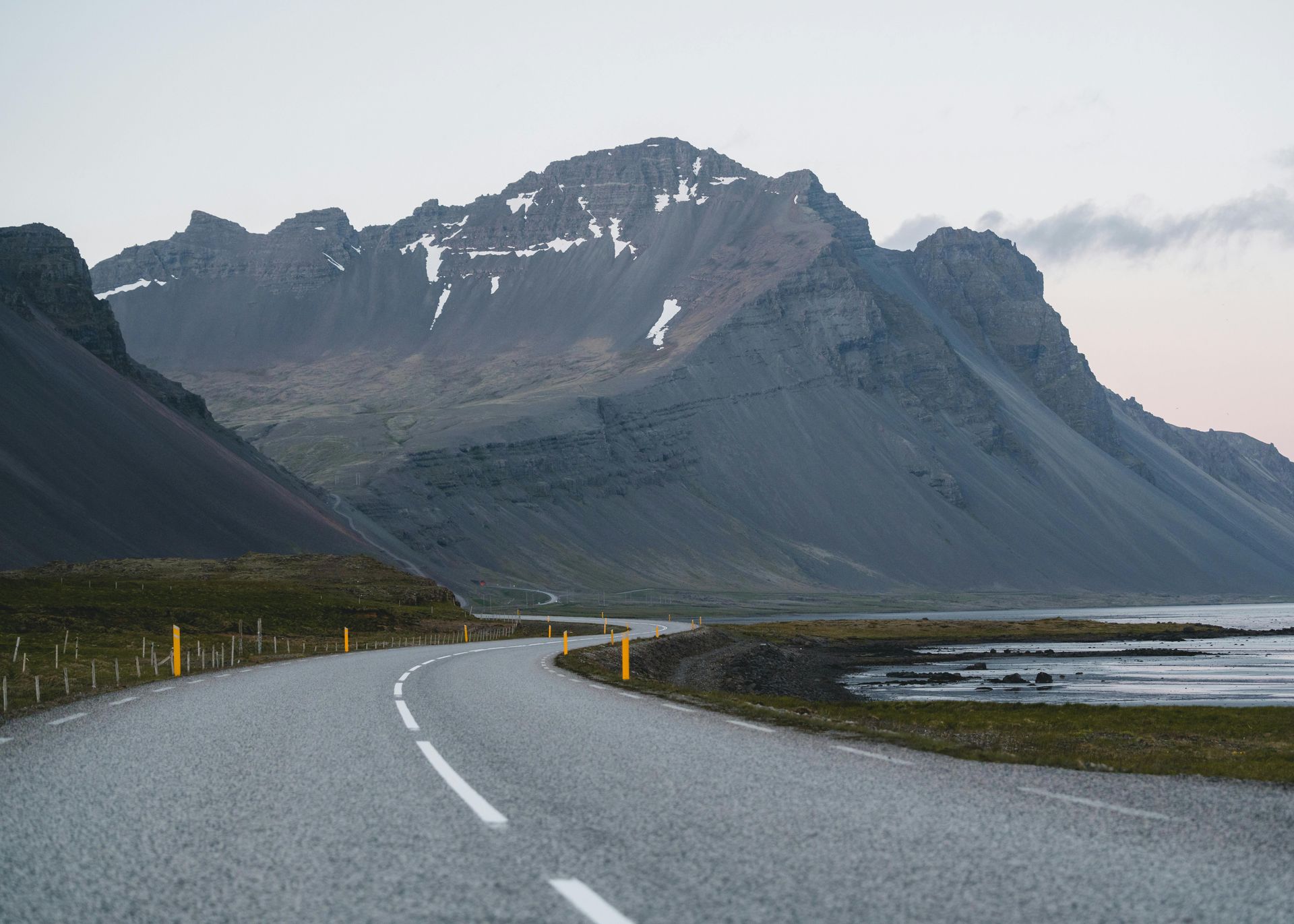 A road with mountains in the background and a lake in the foreground in Iceland.