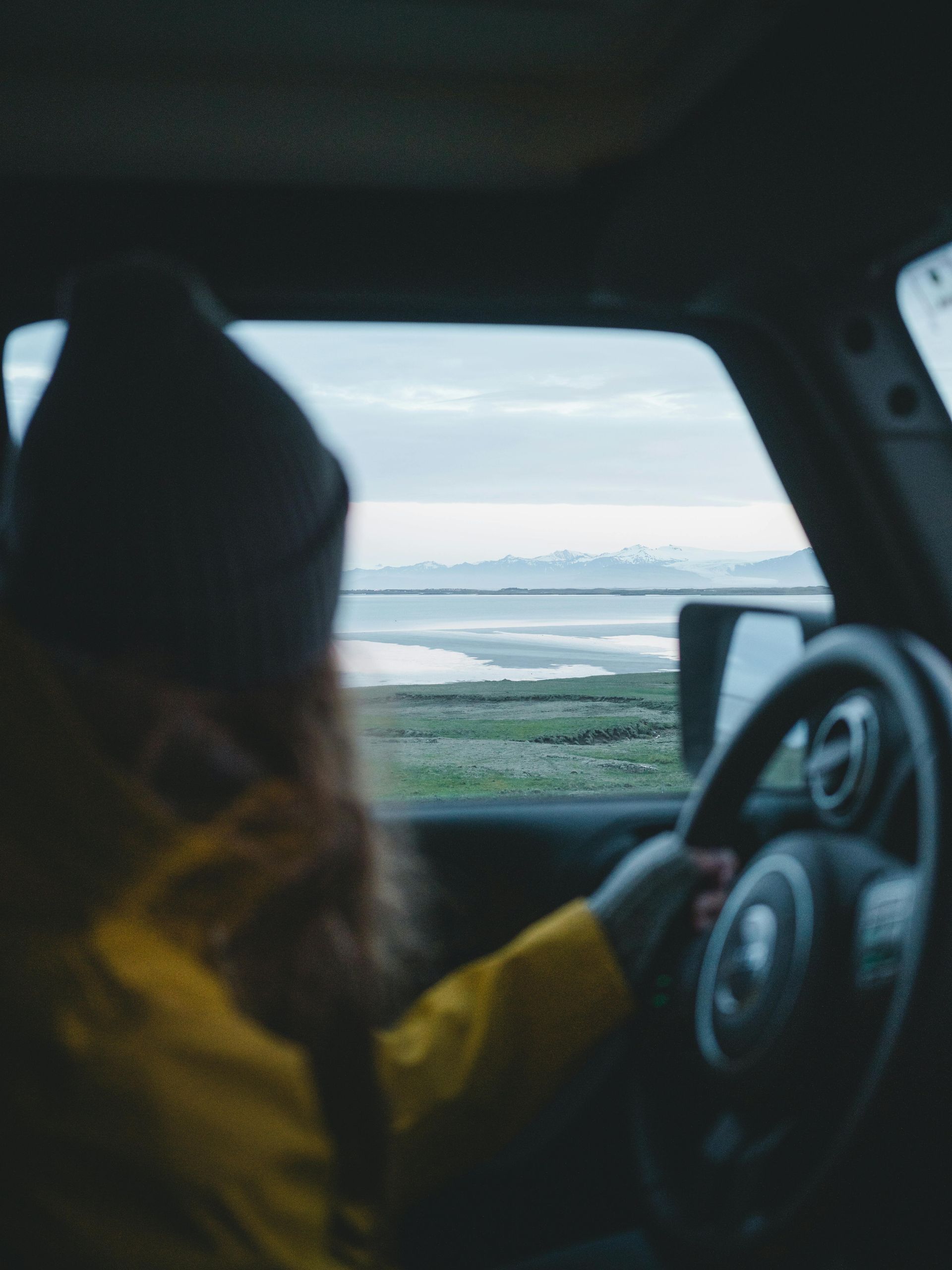 A woman in a yellow jacket is driving a car in Iceland.