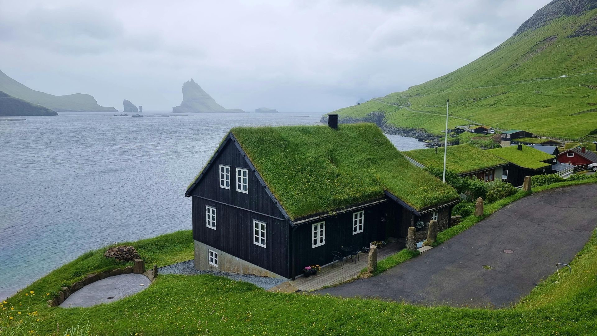 A small white house with a thatched roof is sitting on top of a hill on the Faroe Islands.