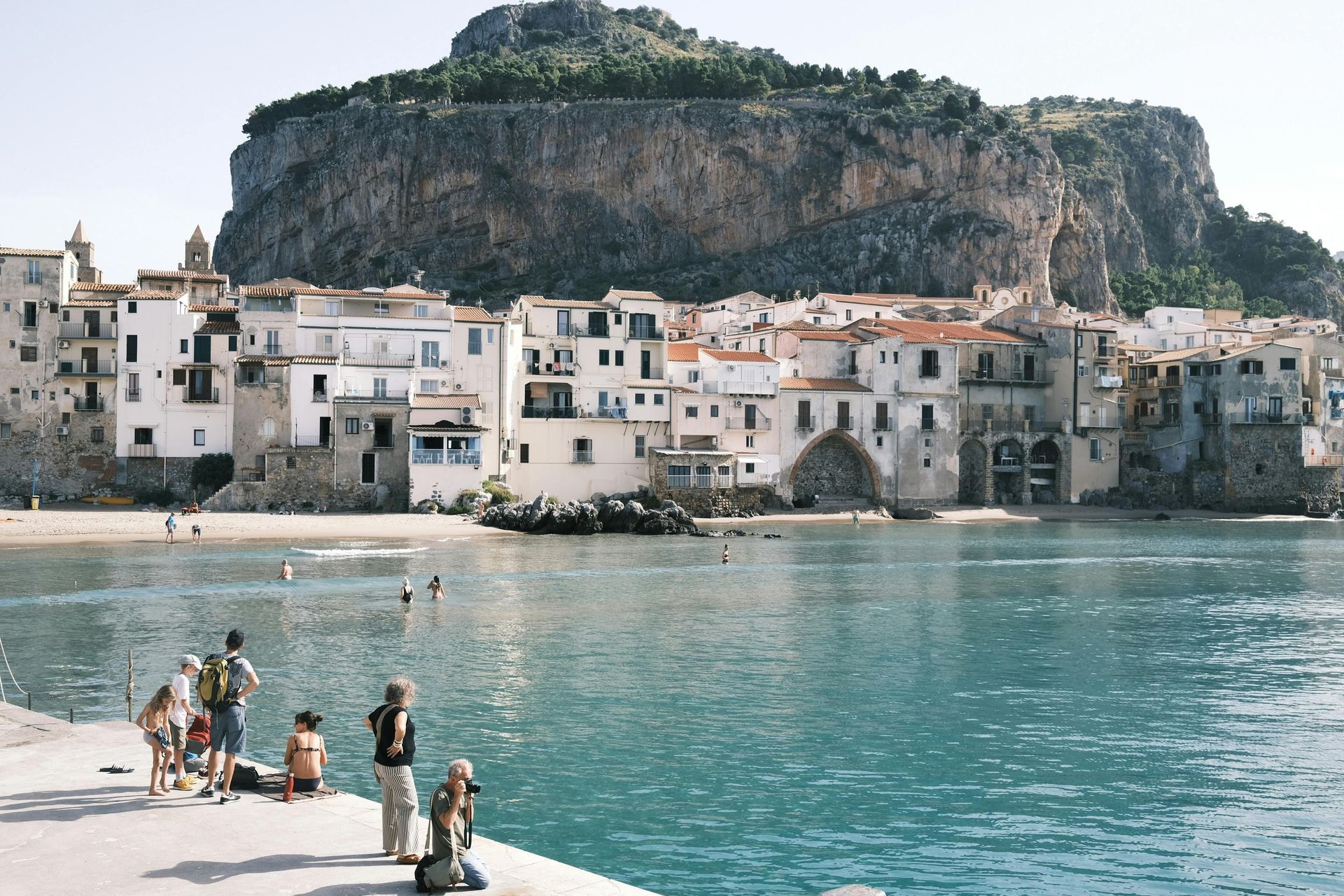 A group of people are standing on a pier overlooking a body of water in Sicily, Italy.