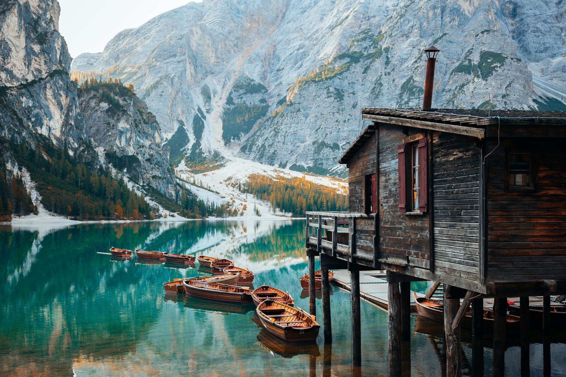 A wooden house is sitting on stilts in the middle of a lake surrounded The Dolomites in Italy.