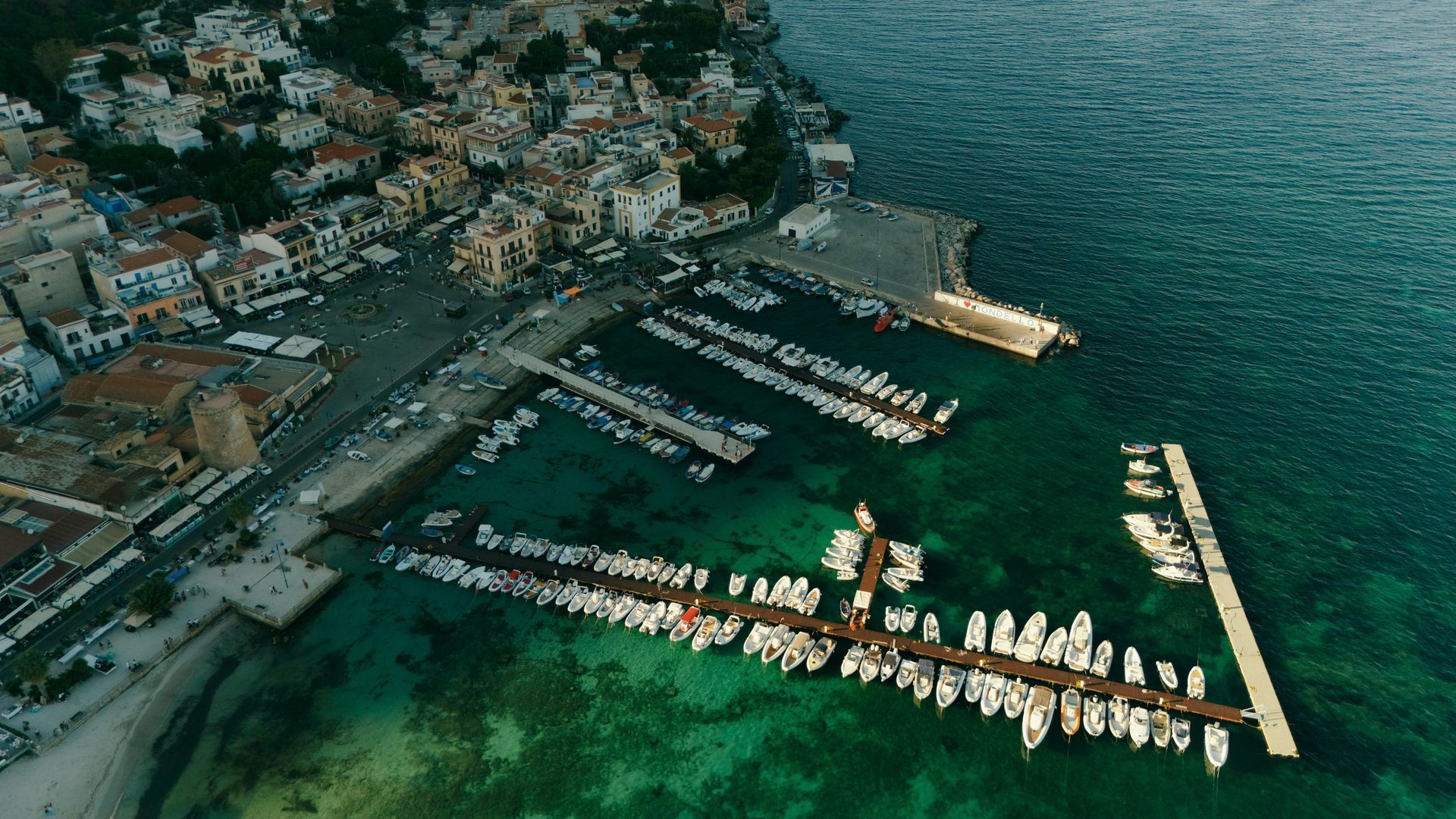 An aerial view of a marina with boats docked and a city in the background in Sicily, Italy.